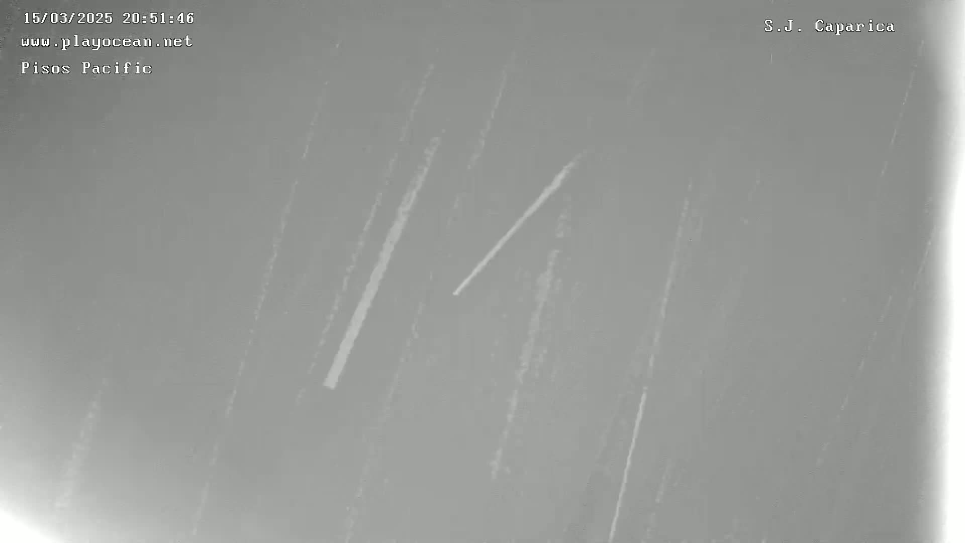 A grayscale image shows several faint, white streaks against a muted gray background, possibly depicting light trails in an overcast sky.