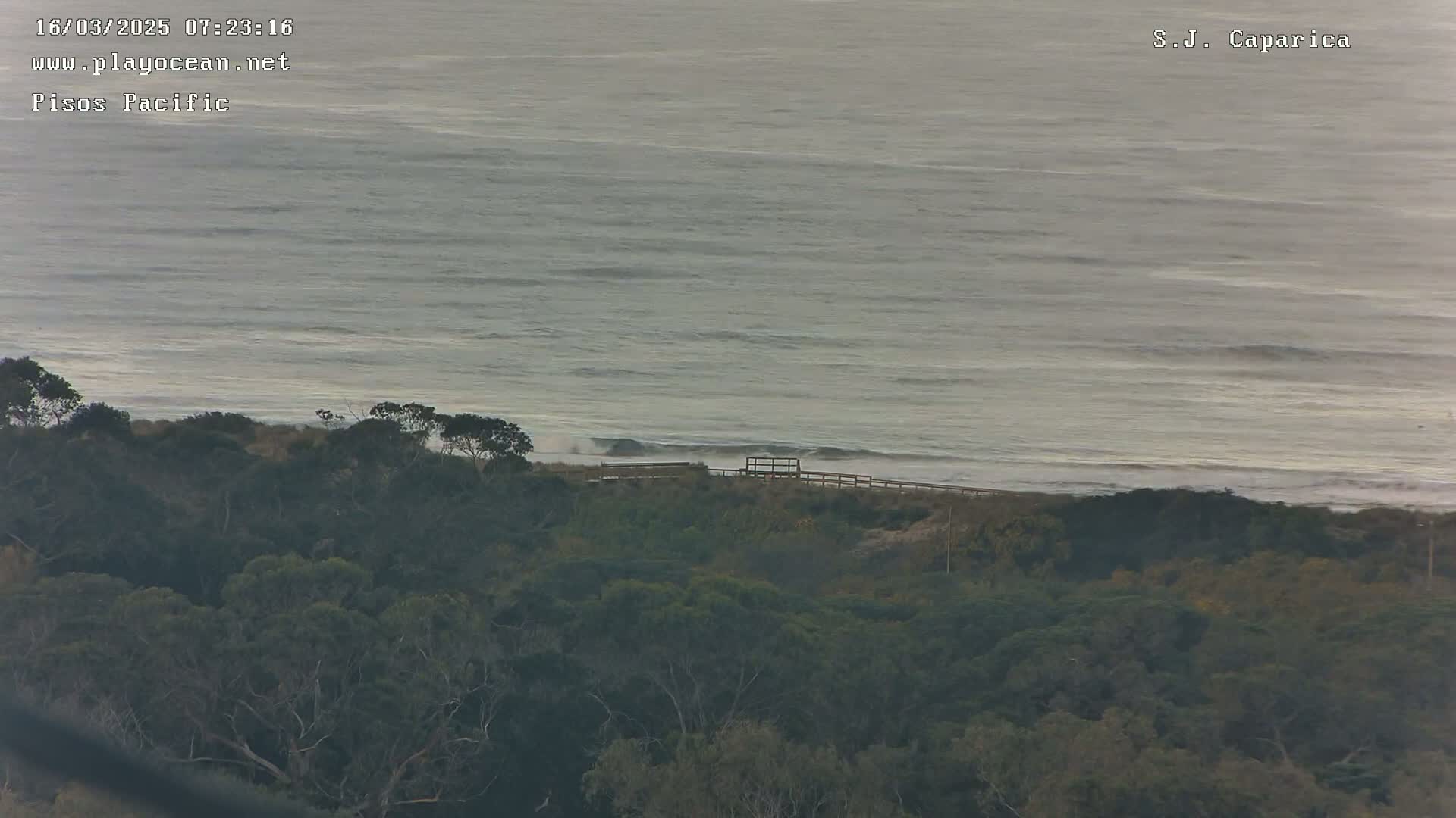 A calm, gray ocean meets a dark green coastline with a small wooden structure visible near the shore.