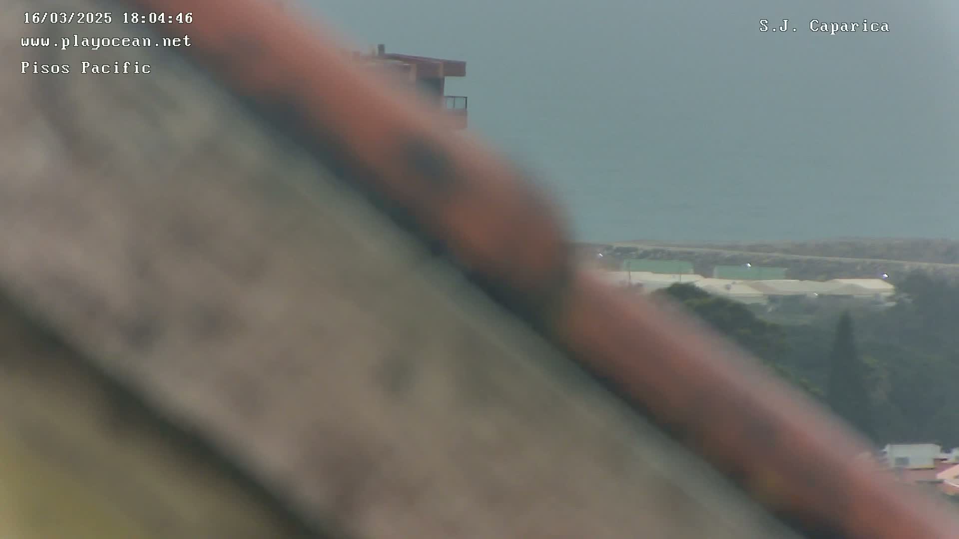 A blurry view of a coastal scene on an overcast day shows a building in the midground and a distant ocean with a shoreline.