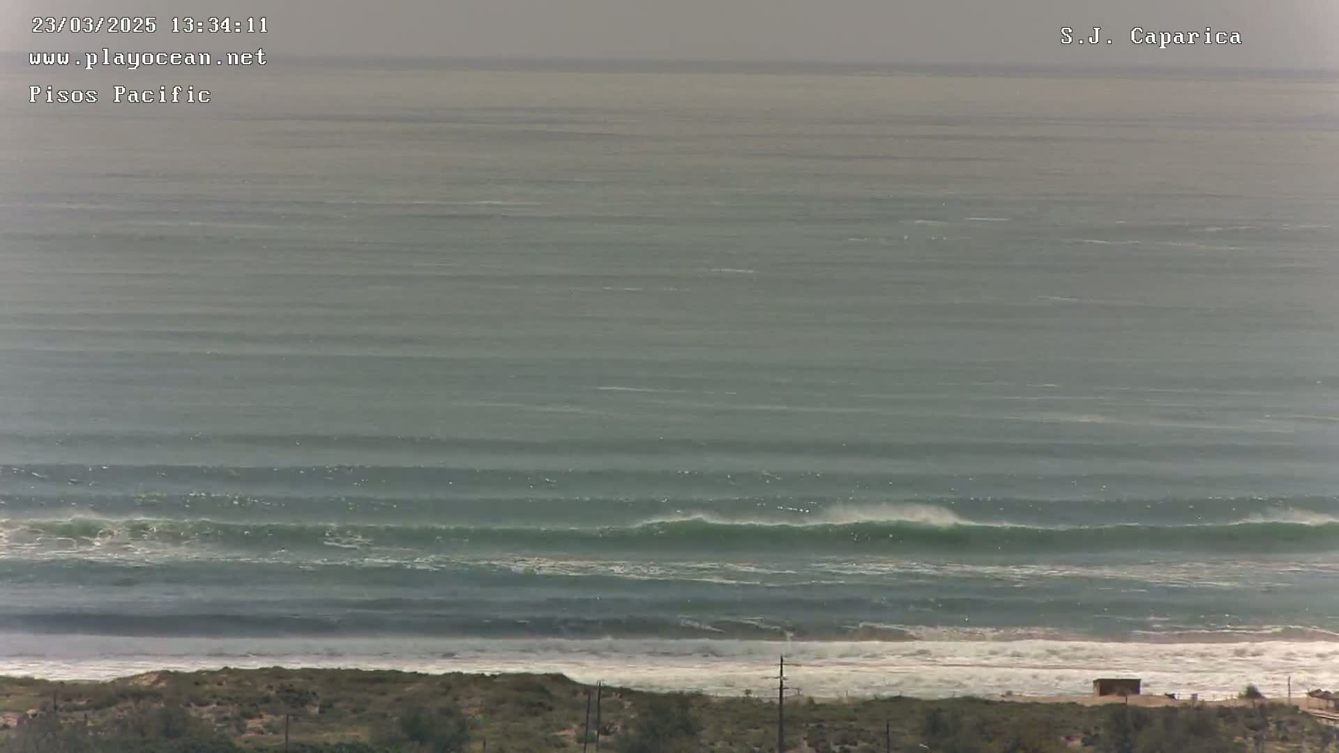 A long shot of an ocean with moderate waves breaking near a shoreline under an overcast sky.