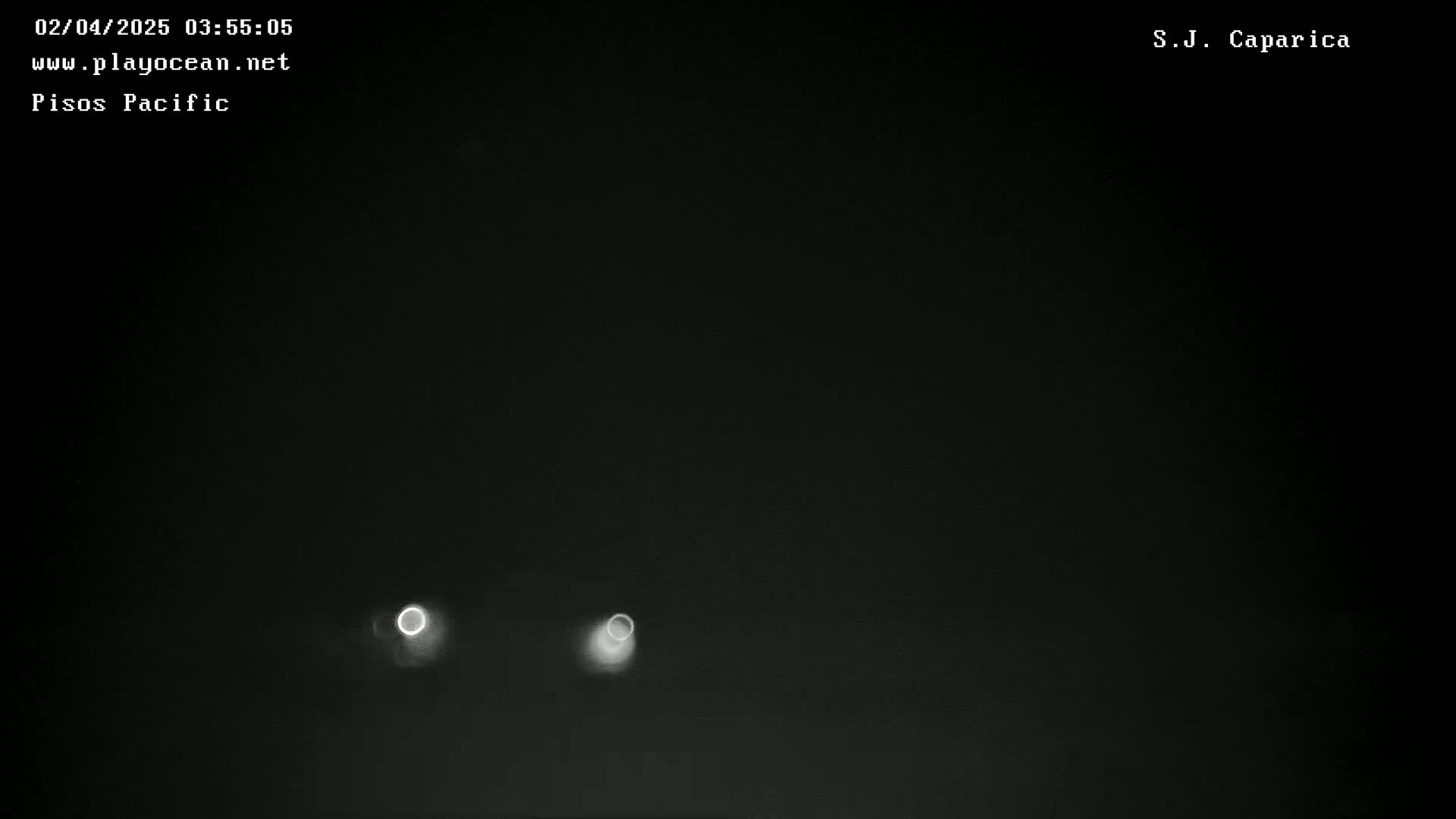 A nighttime, dark image shows two distant, bright lights, likely headlights, in a hazy or foggy atmosphere.