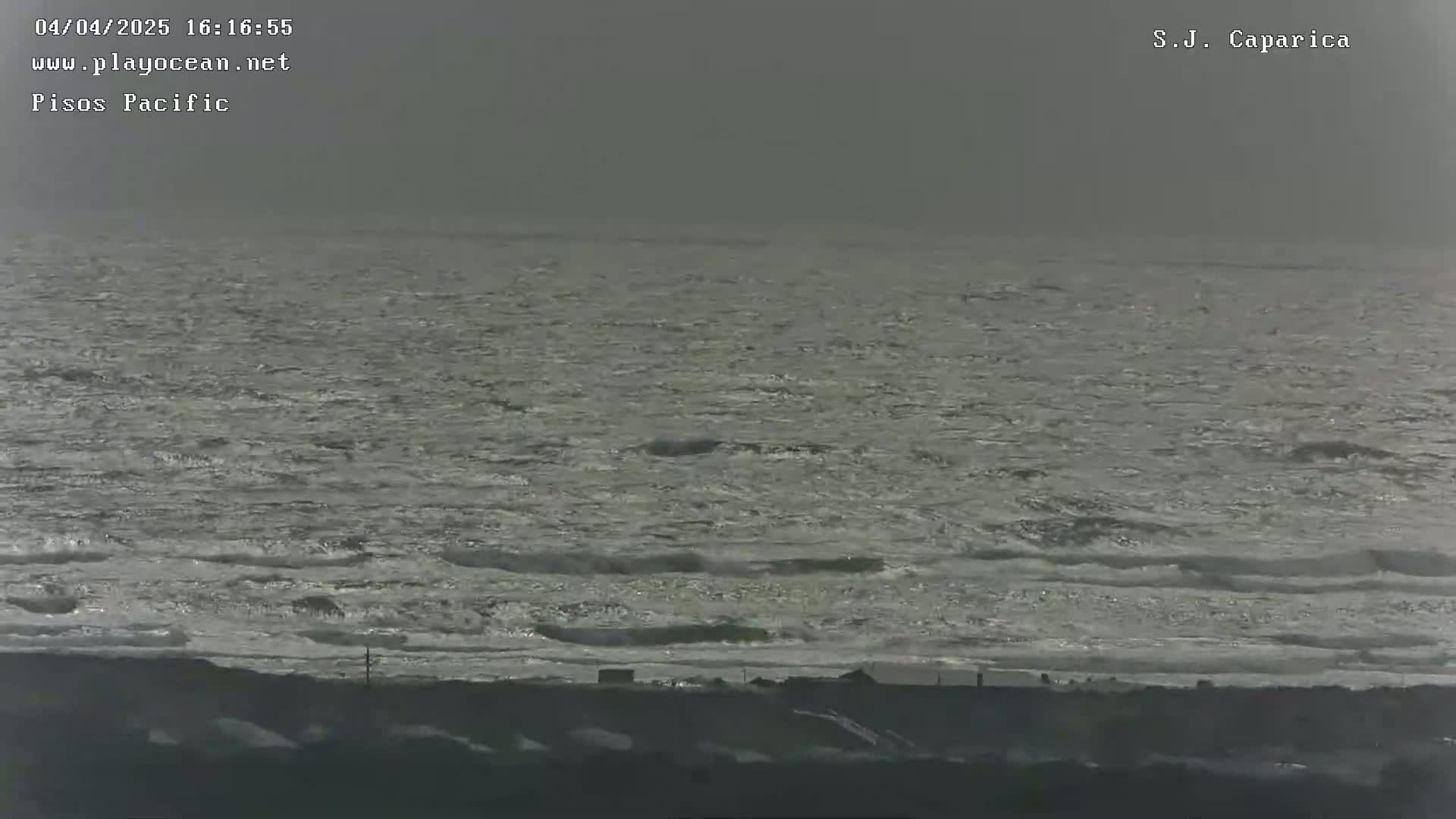 A gray, overcast sky hangs over a choppy ocean meeting a dark shoreline.