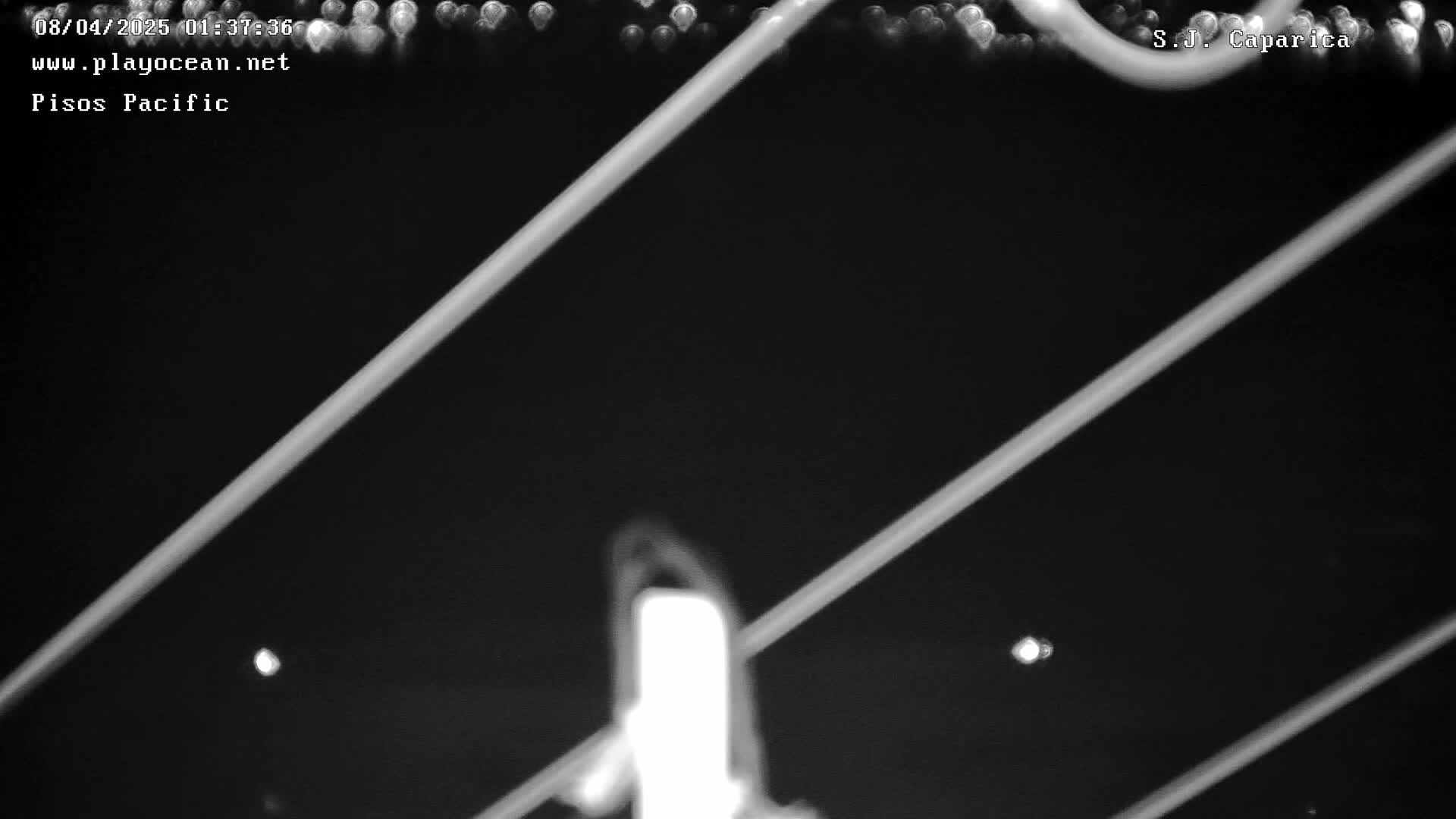 A nighttime, blurry image shows several bright, diagonal lines intersecting a central, bright, vertical line, with faint, distant lights visible in the dark background.