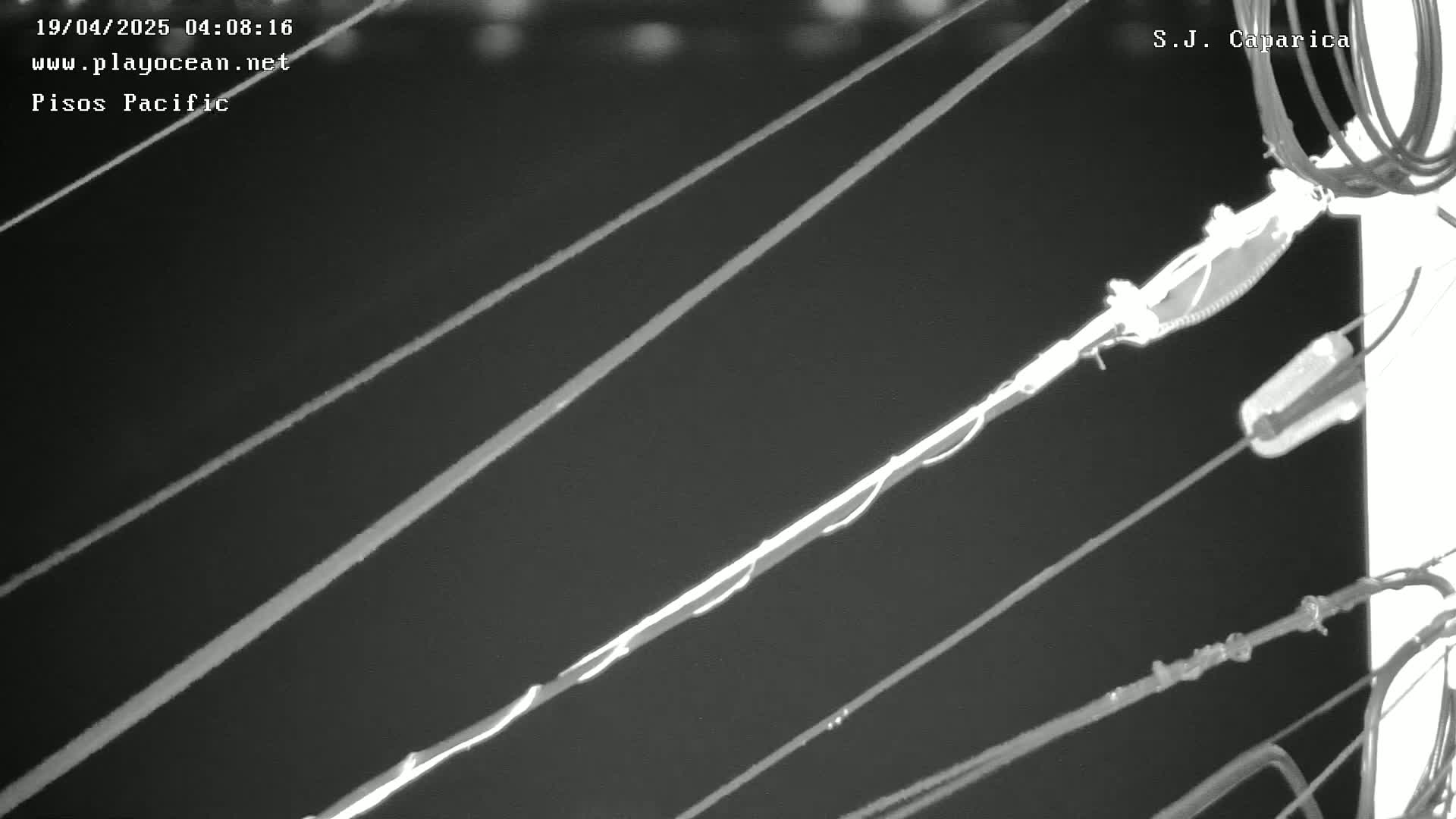 A nighttime, low-light image shows several diagonal wires and cables attached to a pole.