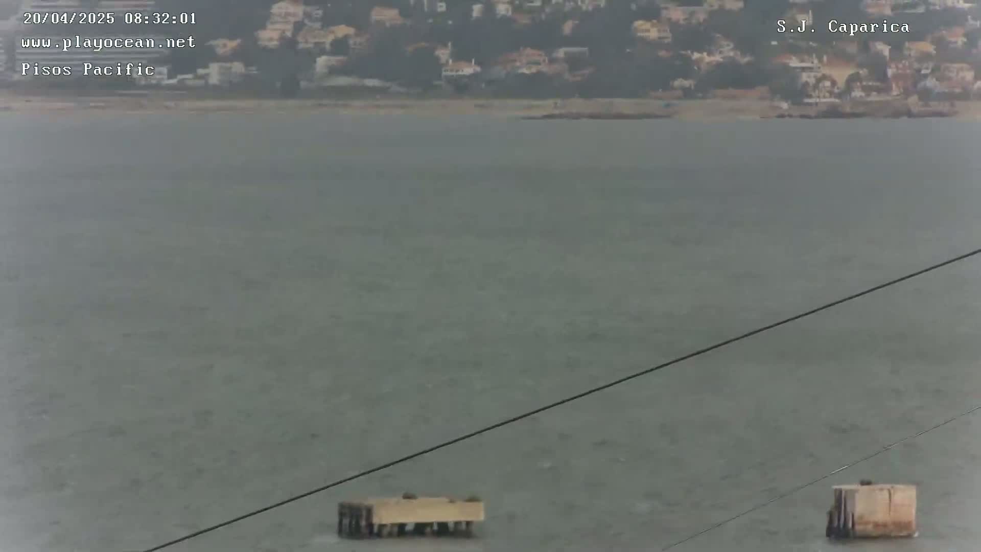 A calm, gray body of water with two small structures visible near the bottom, and a distant shoreline with buildings in the background.