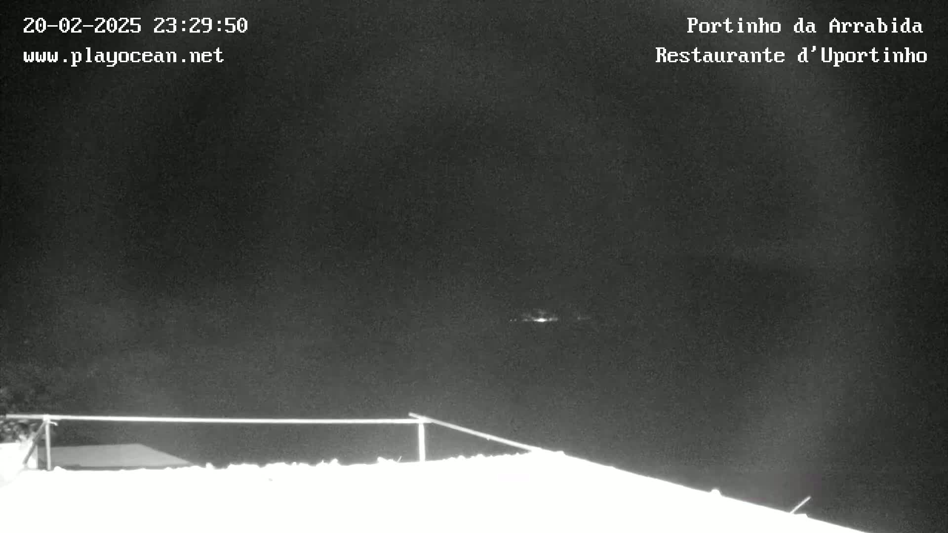A nighttime, low-light image shows a dark sky over a snow-covered surface with a railing in the foreground.