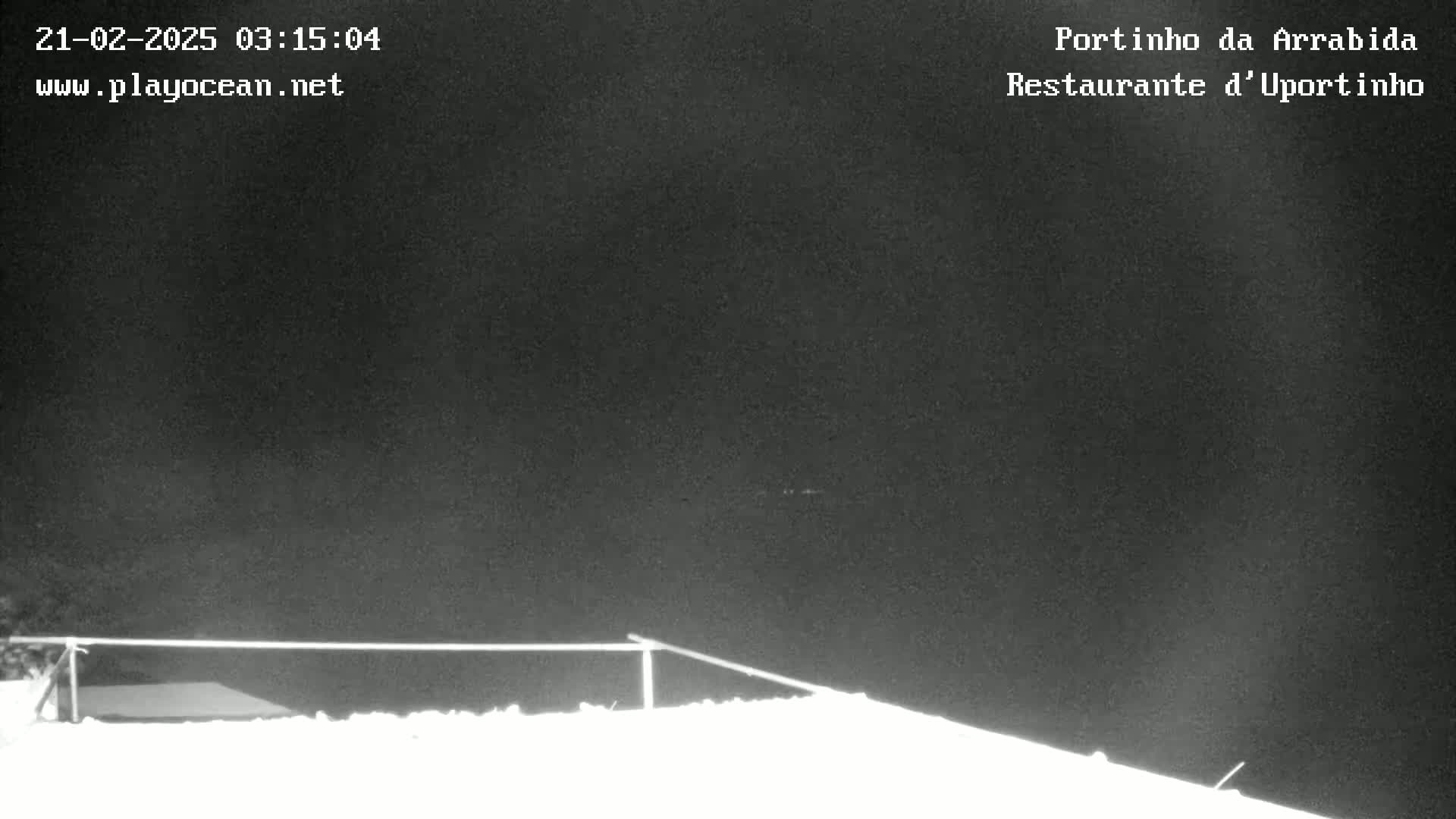 A nighttime, snow-covered scene shows a low-lying metal railing against a dark sky.