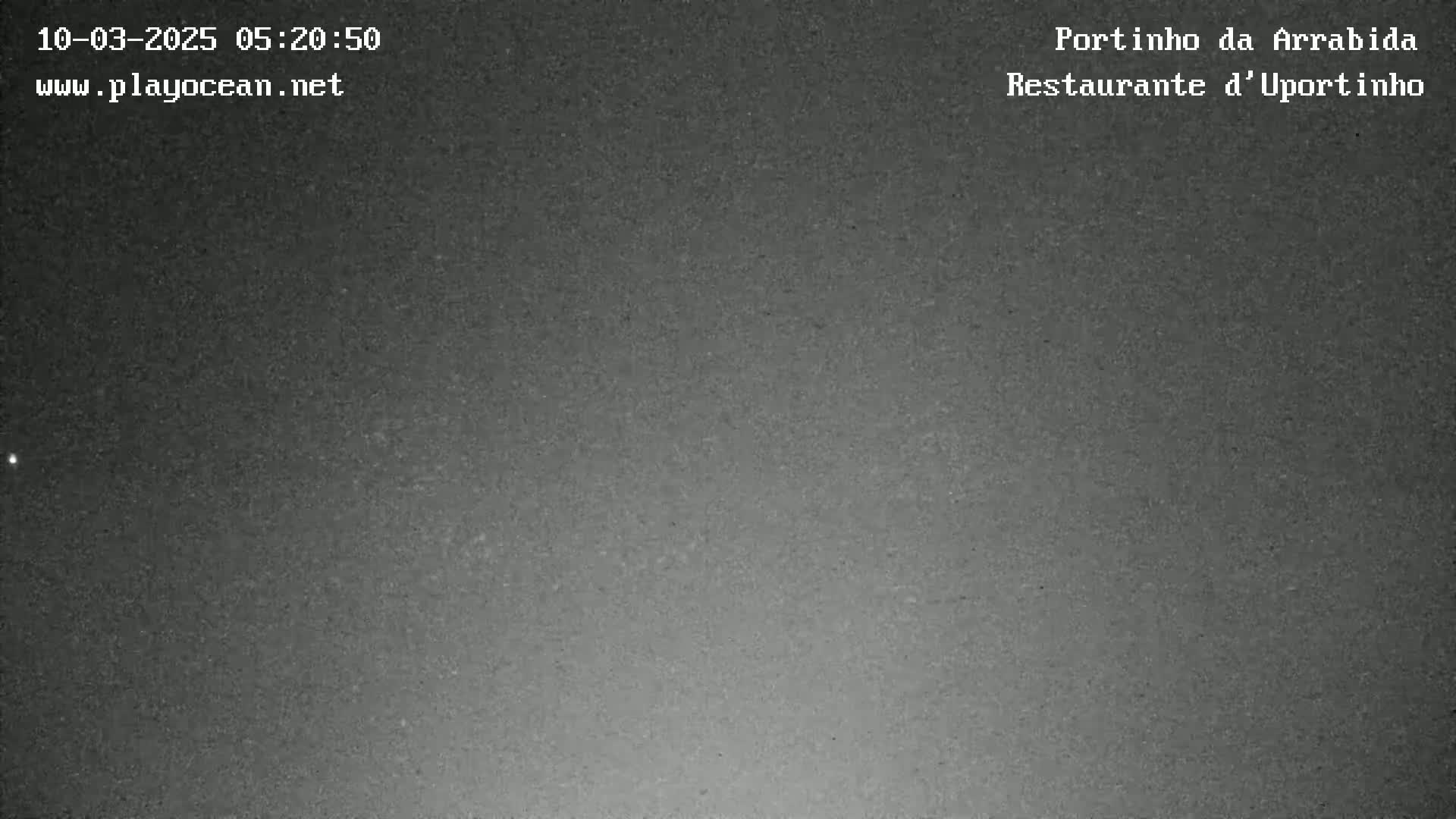 A dark, grainy nighttime image shows a mostly clear sky with a faint light source near the bottom.