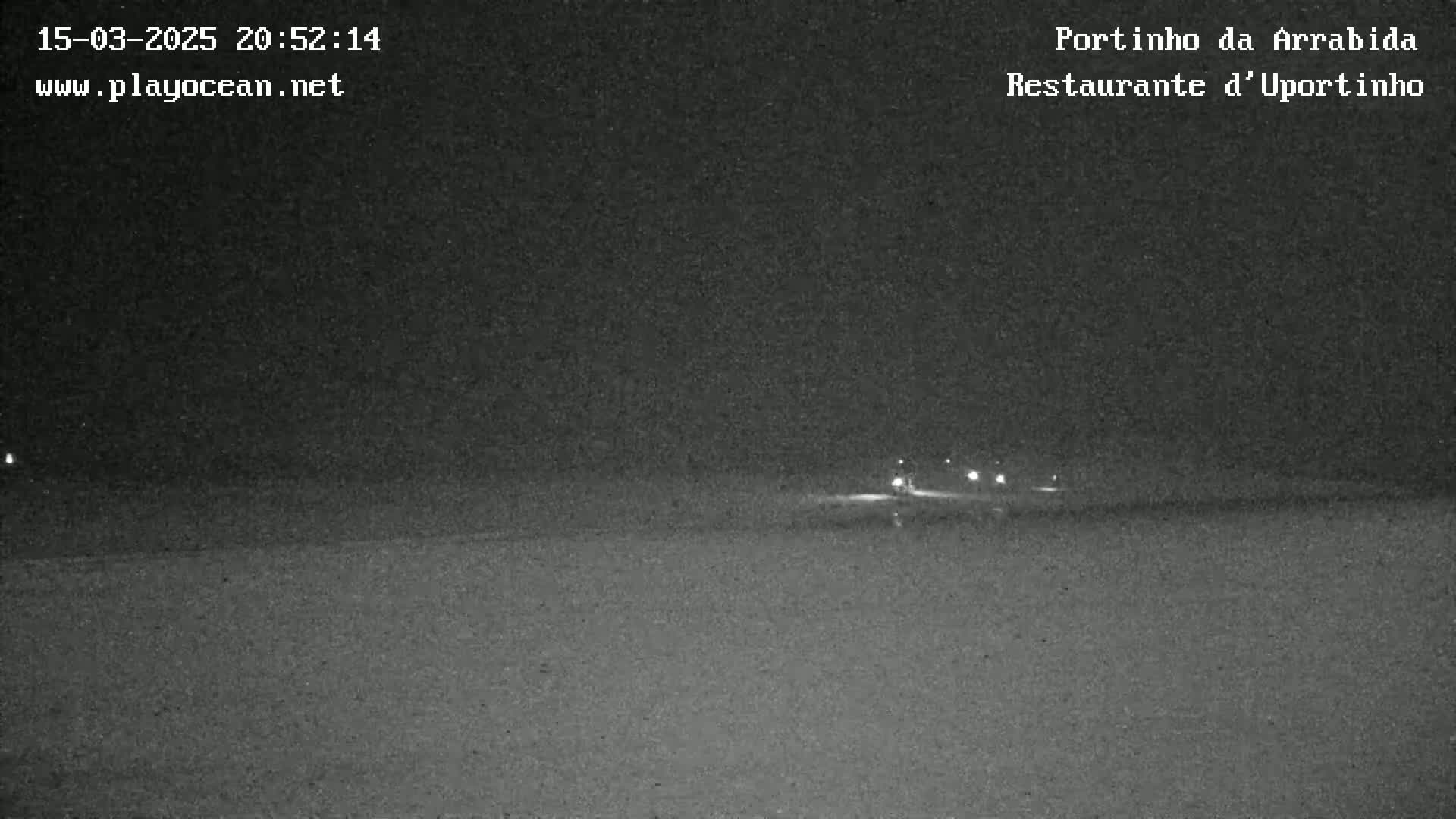 A nighttime, low-light image shows a dark beach with a few distant lights visible on the horizon.