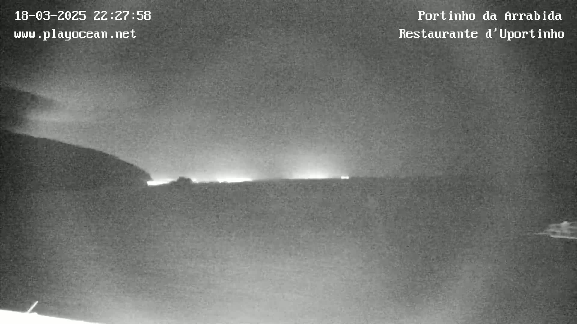A nighttime, low-light image shows a dark landscape with faint lights on the horizon.