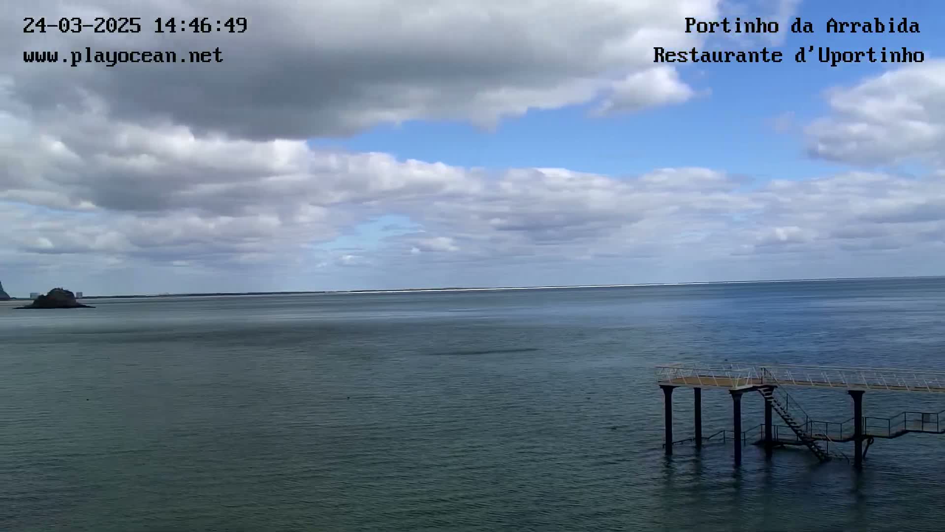 A partly cloudy day shows a calm, dark-blue ocean with a small island in the distance and a simple pier with stairs extending into the water.