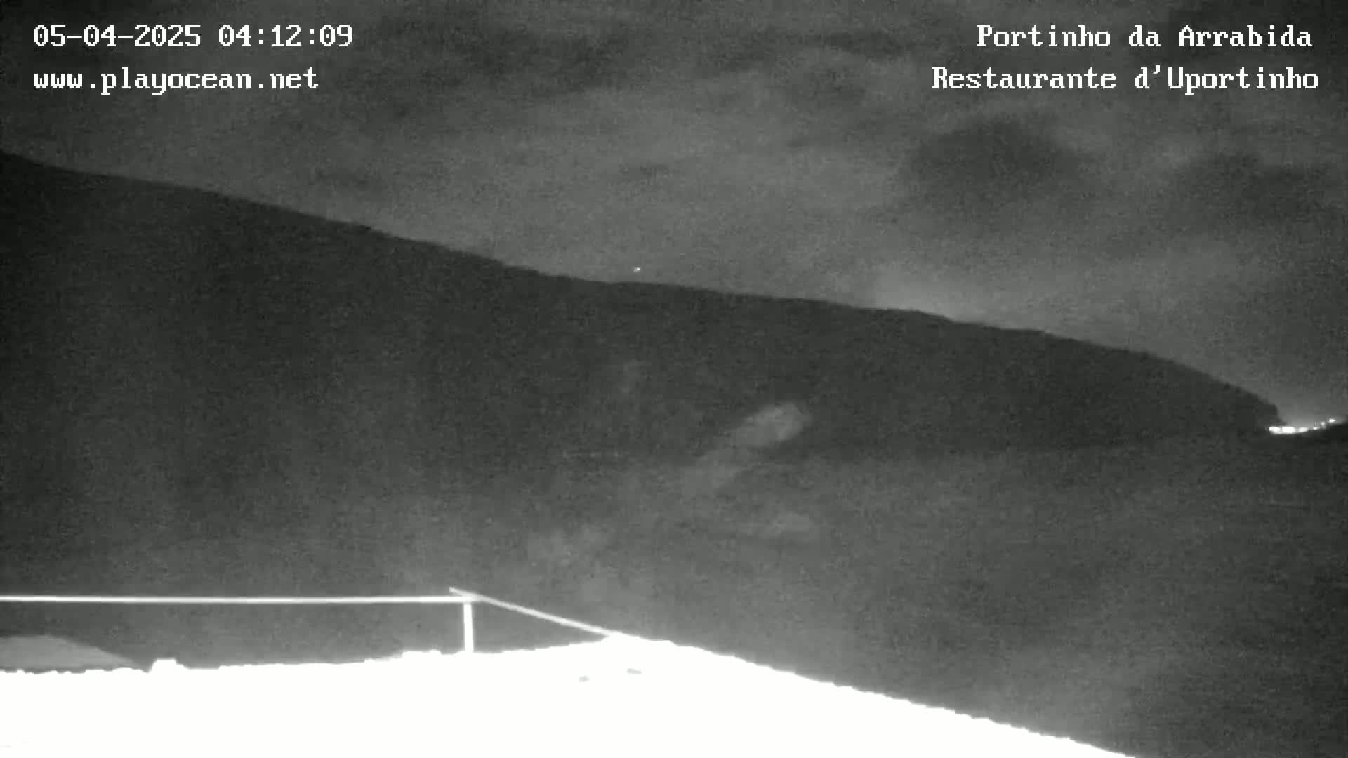 A nighttime, low-light view shows a dark hill or mountain under a cloudy sky.