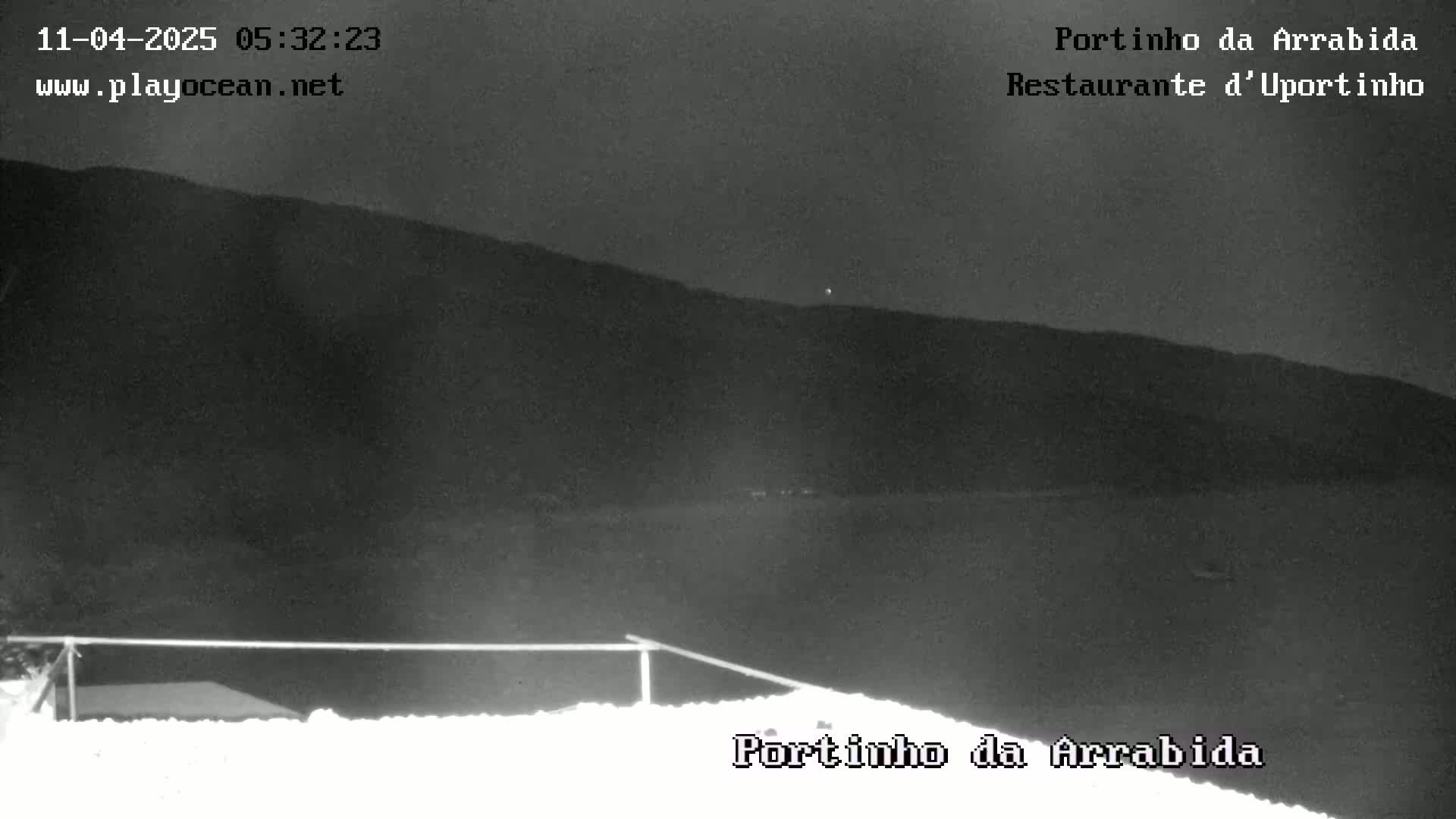A nighttime, low-light image shows a dark body of water at the base of a hill under a mostly clear, dark sky.