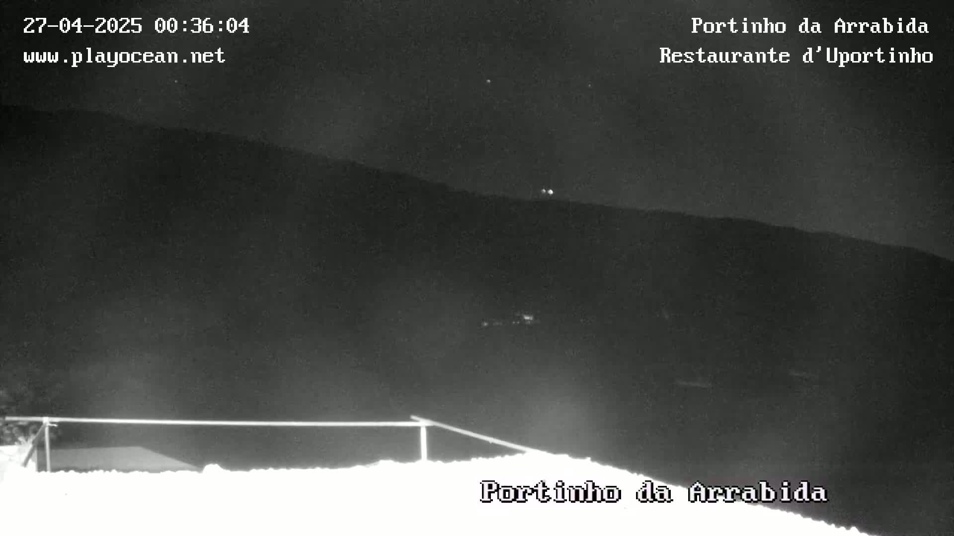 A nighttime view shows dark hills and a low metal railing in the foreground under a clear, dark sky.