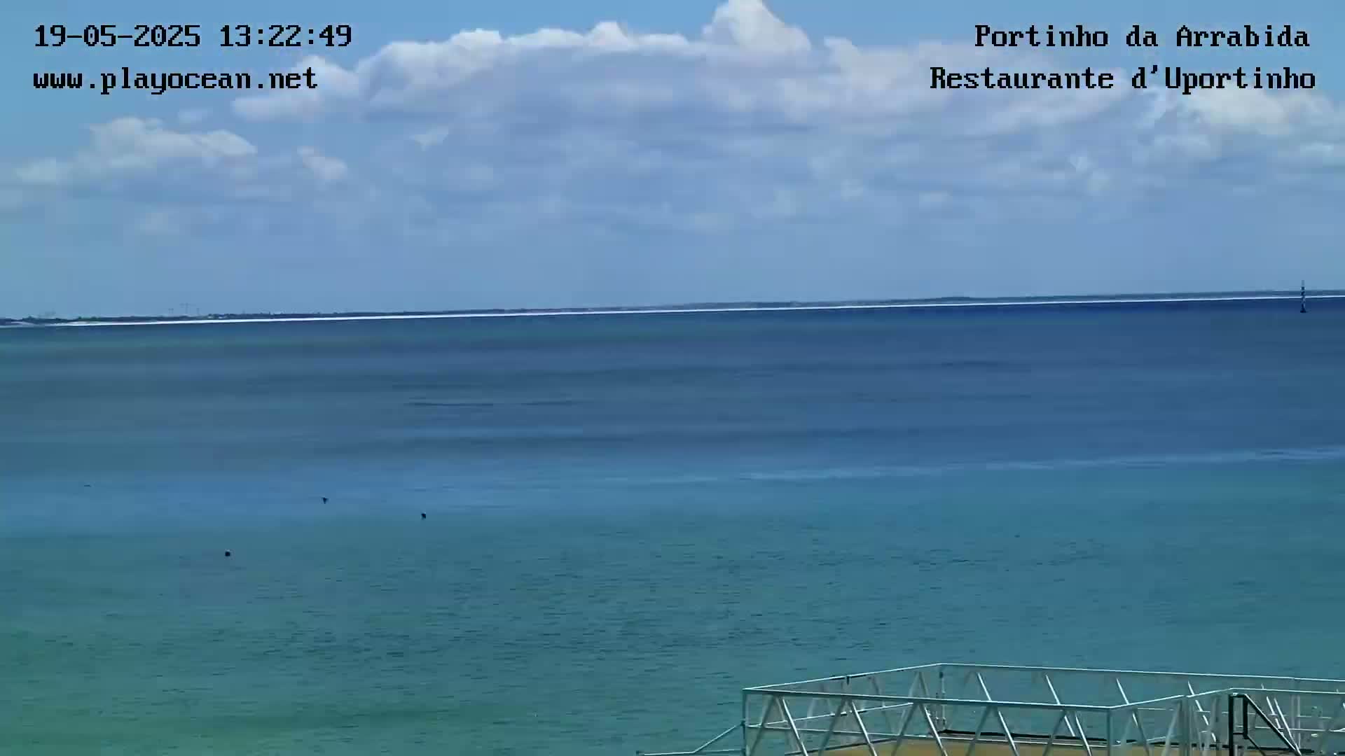 A partly cloudy sky overlooks a calm, teal ocean with a distant shoreline.