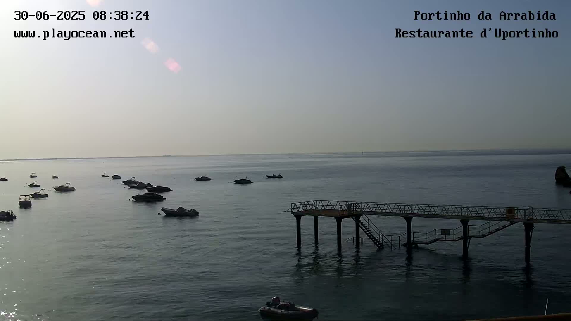 Several small motorboats are moored in calm, gray water near a pier on a hazy day.