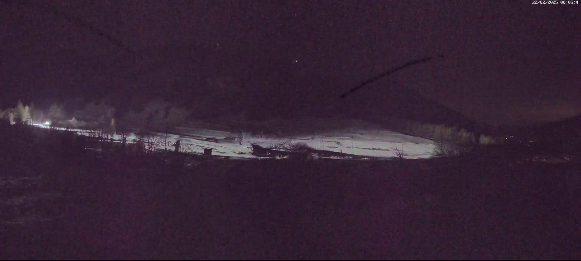 A snow-covered landscape is dimly lit at night under a dark sky.