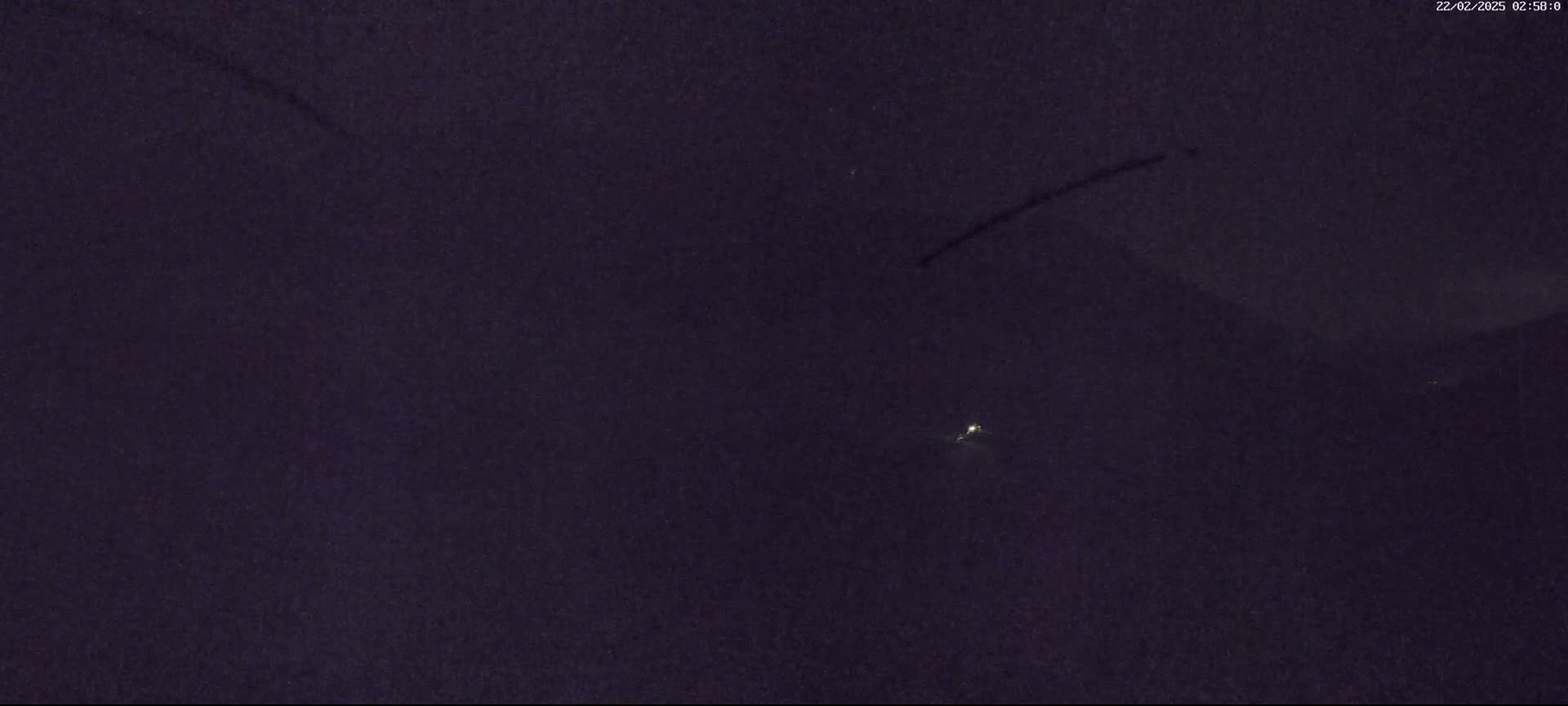 A dark, nighttime scene shows a small, distant light and two faint streaks across a dark sky.