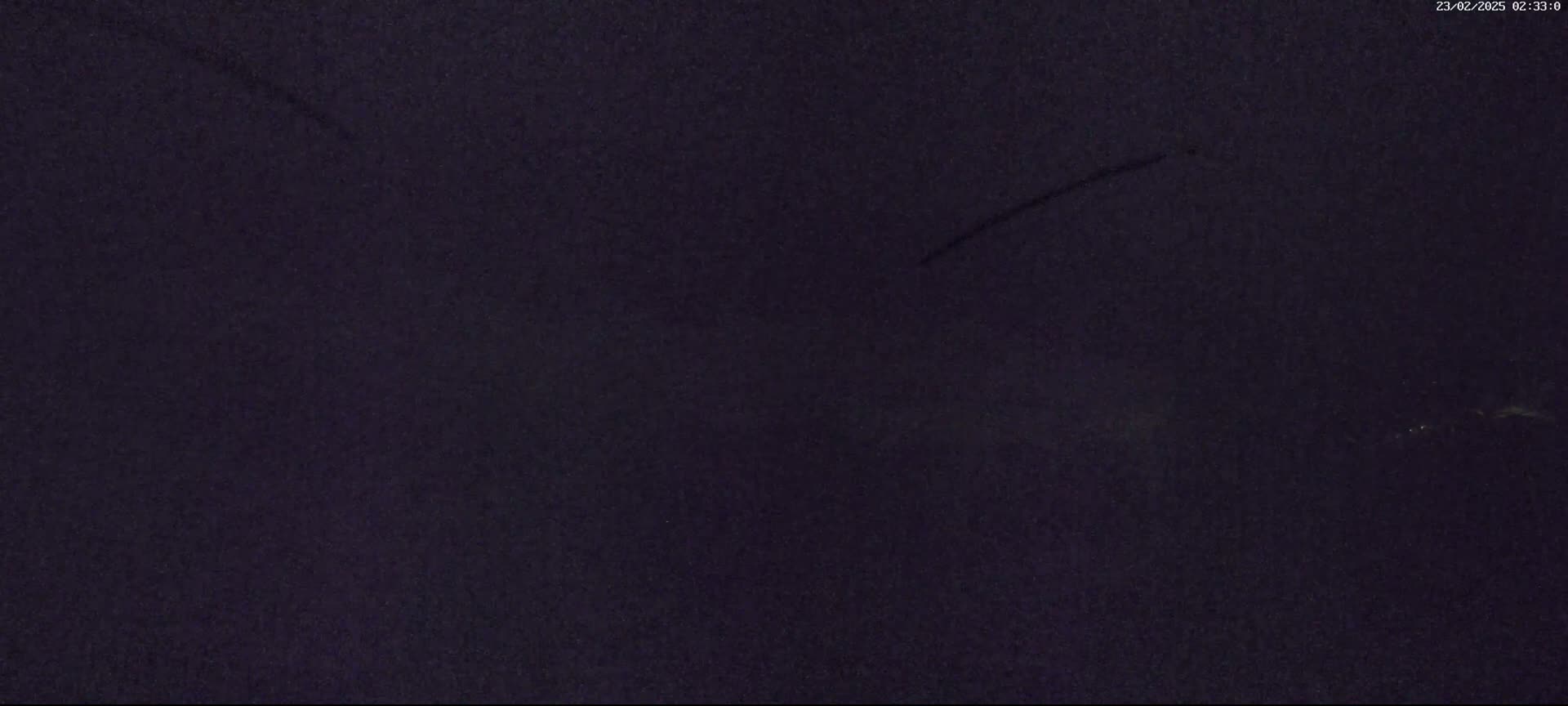 A dark, possibly nighttime, outdoor scene shows a mostly clear sky with a few faint streaks of light near the horizon.