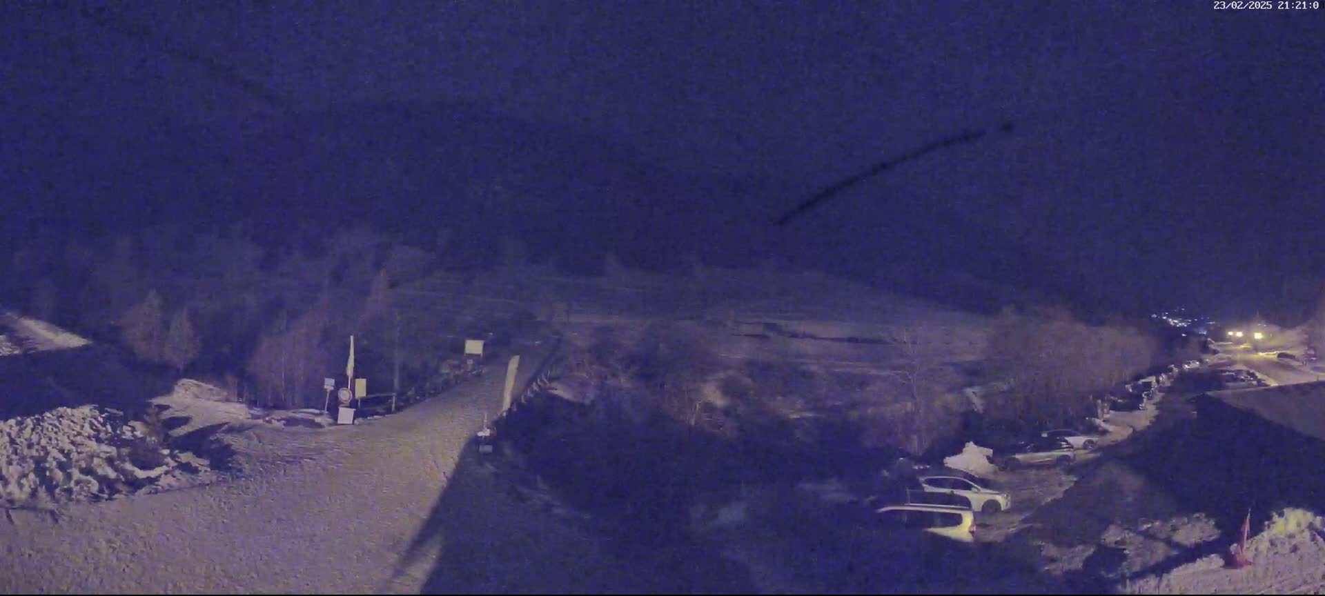 A snow-covered parking lot and road are visible at night under a dark, clear sky, with several cars parked in the lot.