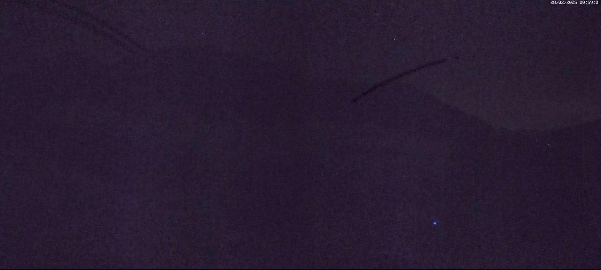A dark purple-toned night sky shows a few faint lights and what appear to be a couple of streaks, possibly from passing aircraft.