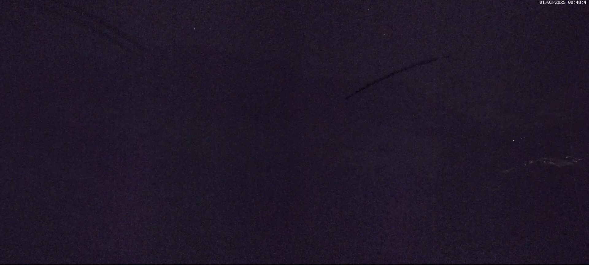 A dark nighttime sky shows two contrails and a faint light source on the horizon.