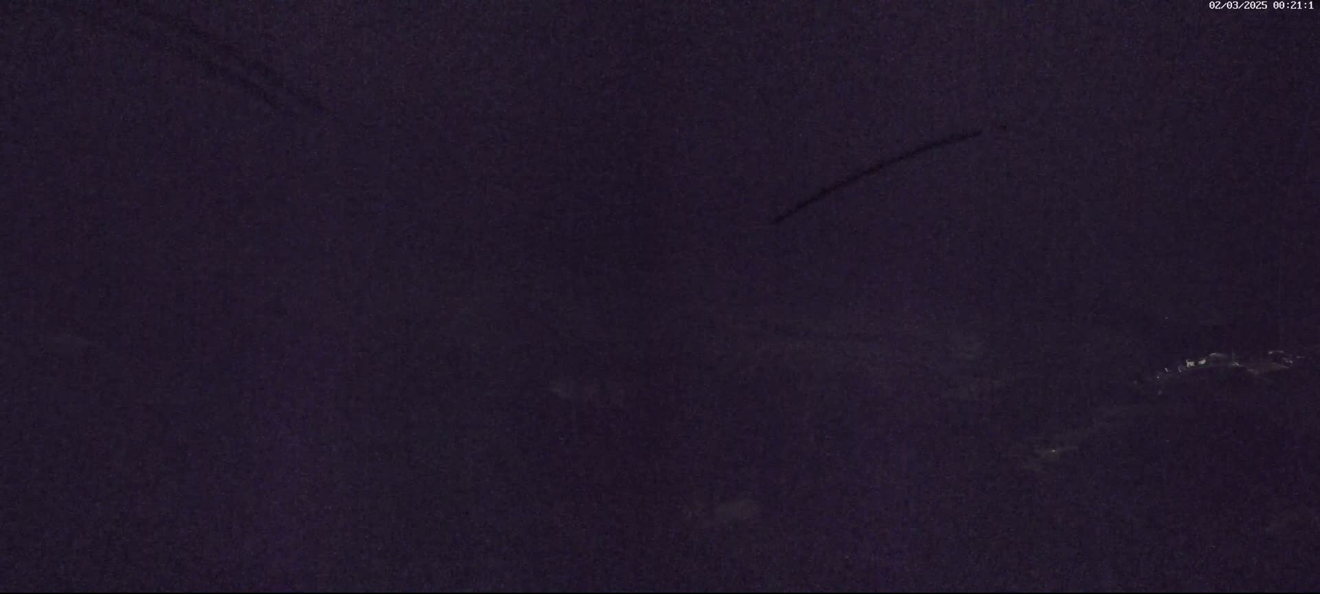 A dark, nighttime scene shows a few faint lights in the distance.