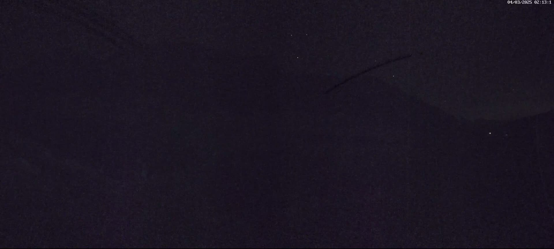 A dark night sky shows a few stars and what appears to be a plane's contrail.