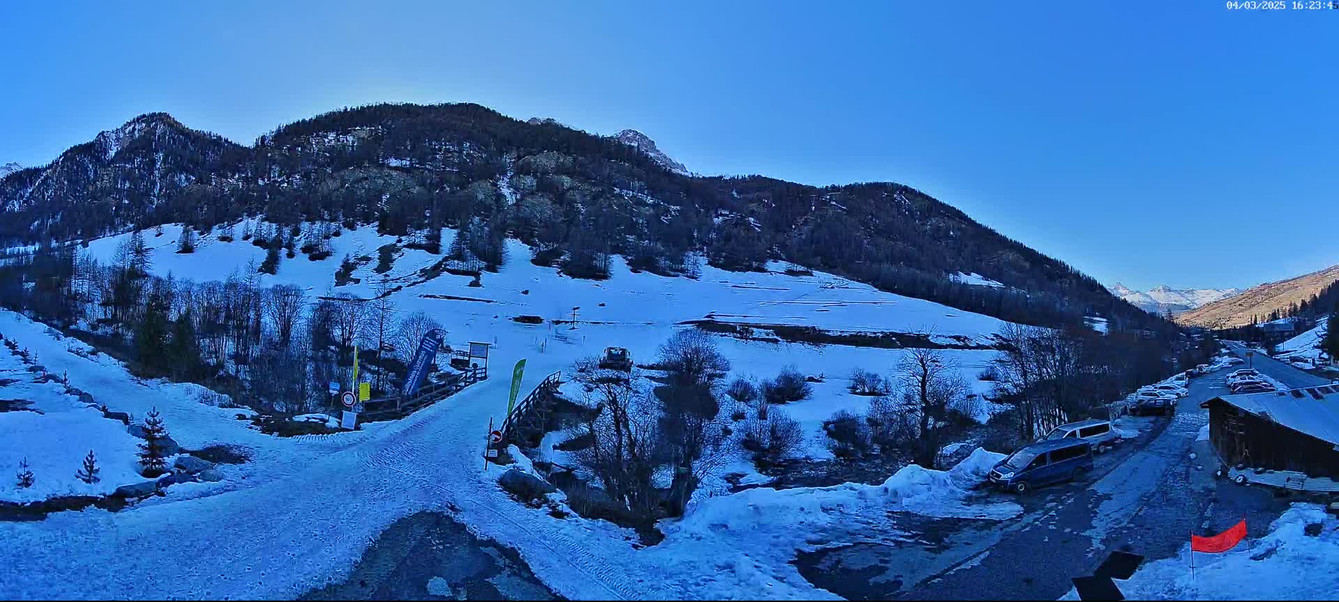 A snow-covered mountainside with a few vehicles parked near a building, under a clear blue sky.