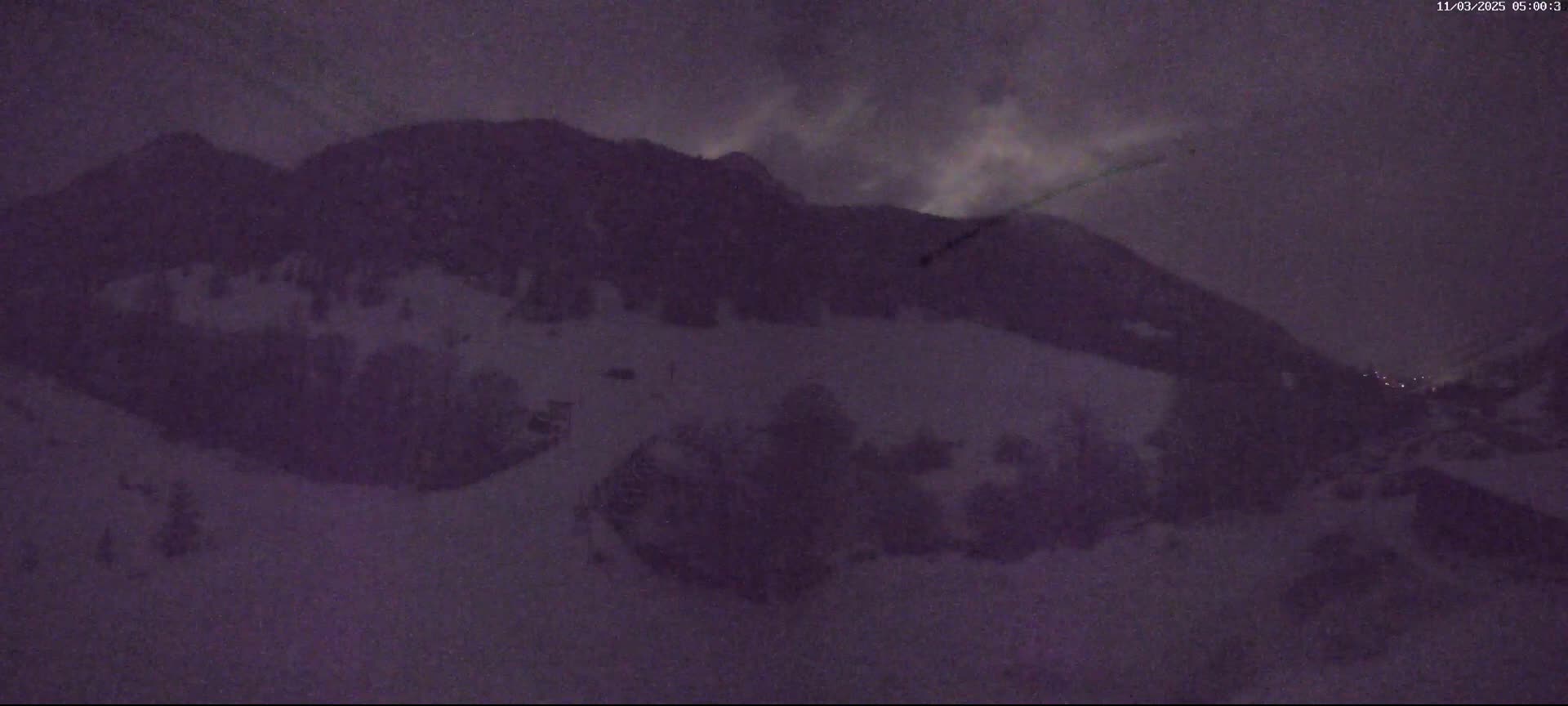 A snow-covered mountainside is visible under a dark, cloudy night sky.