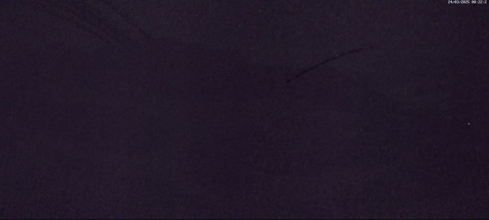 A dark, possibly nighttime, sky shows a faint streak, possibly from a meteor.