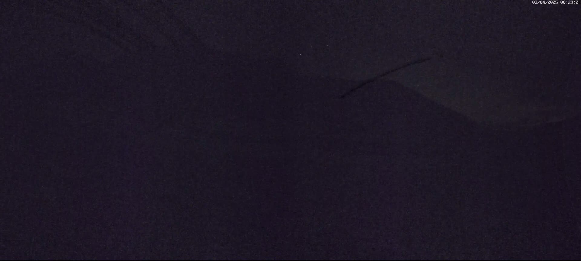 A dark, nighttime image shows a mostly featureless dark purple-grey sky with a faint, thin line across it.