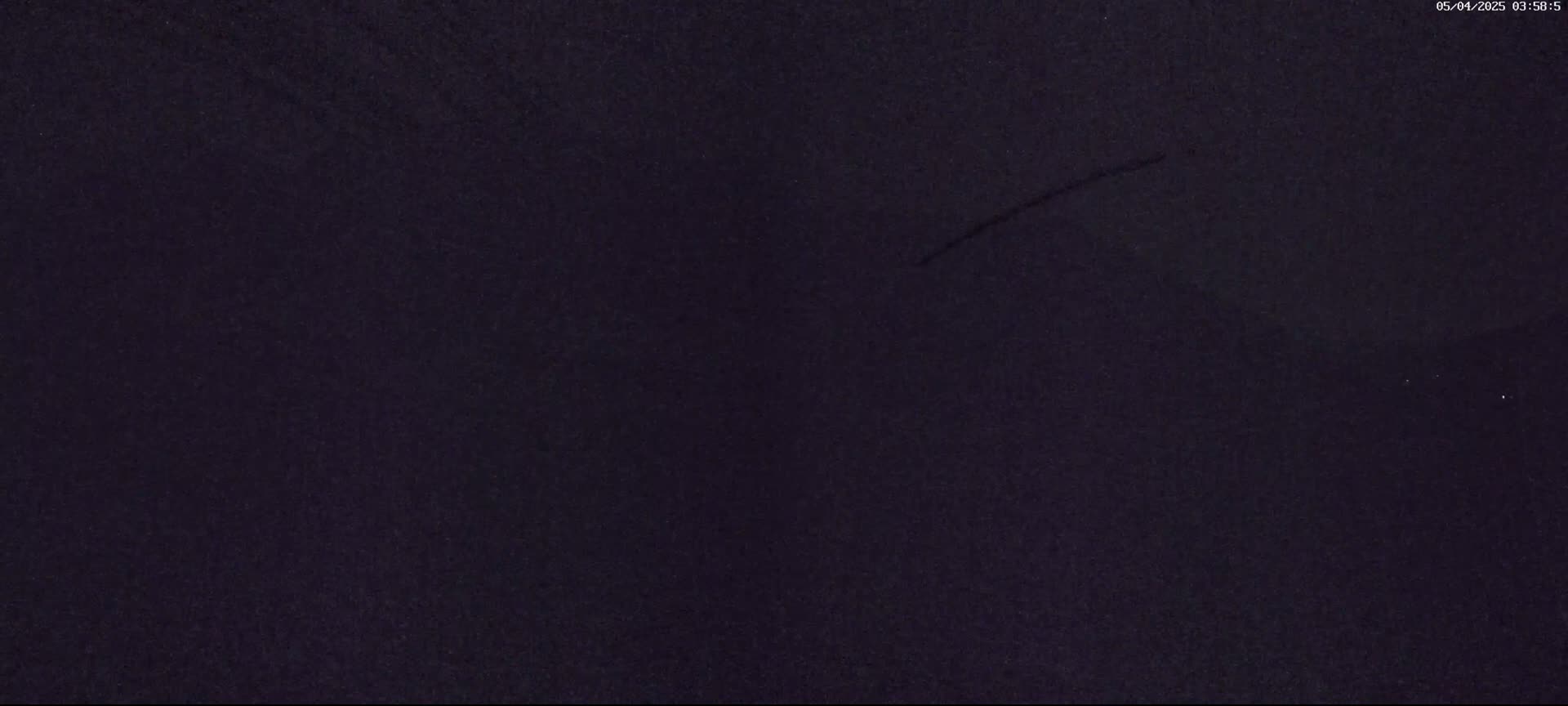 A dark, possibly nighttime, image shows a uniformly dark-colored surface with a few faint, thin streaks.