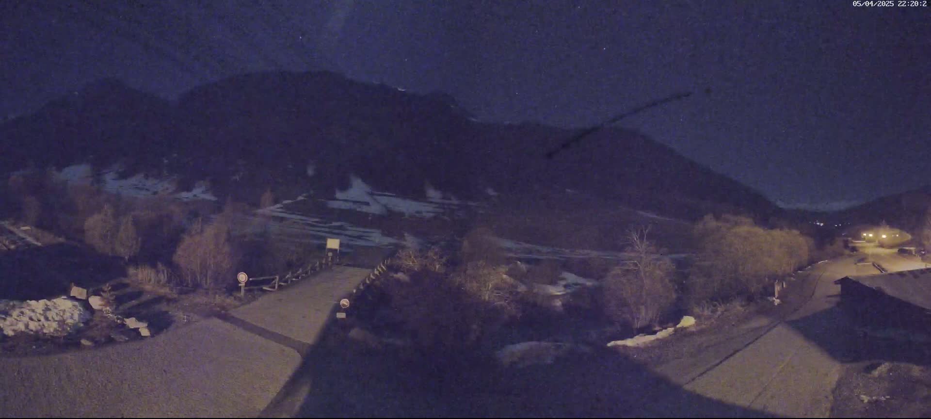 A nighttime view of a mountainside road leading to a small village under a dark, clear sky.