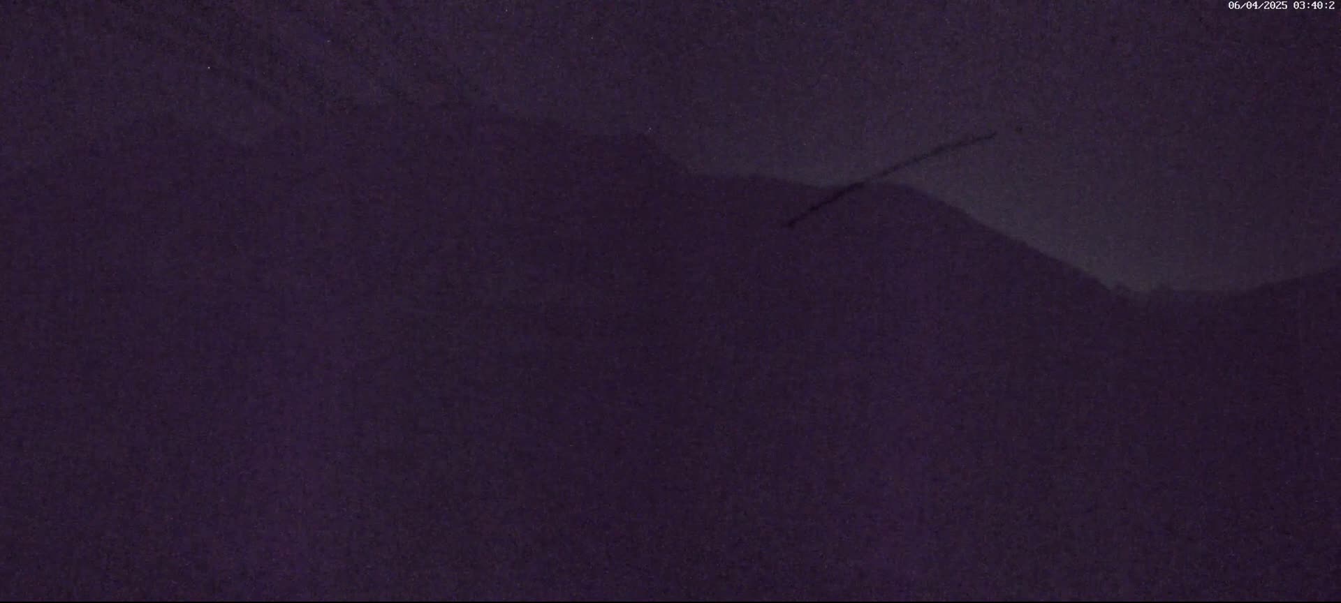 A dark purple, hazy night scene shows a silhouetted mountain range under a mostly clear sky.