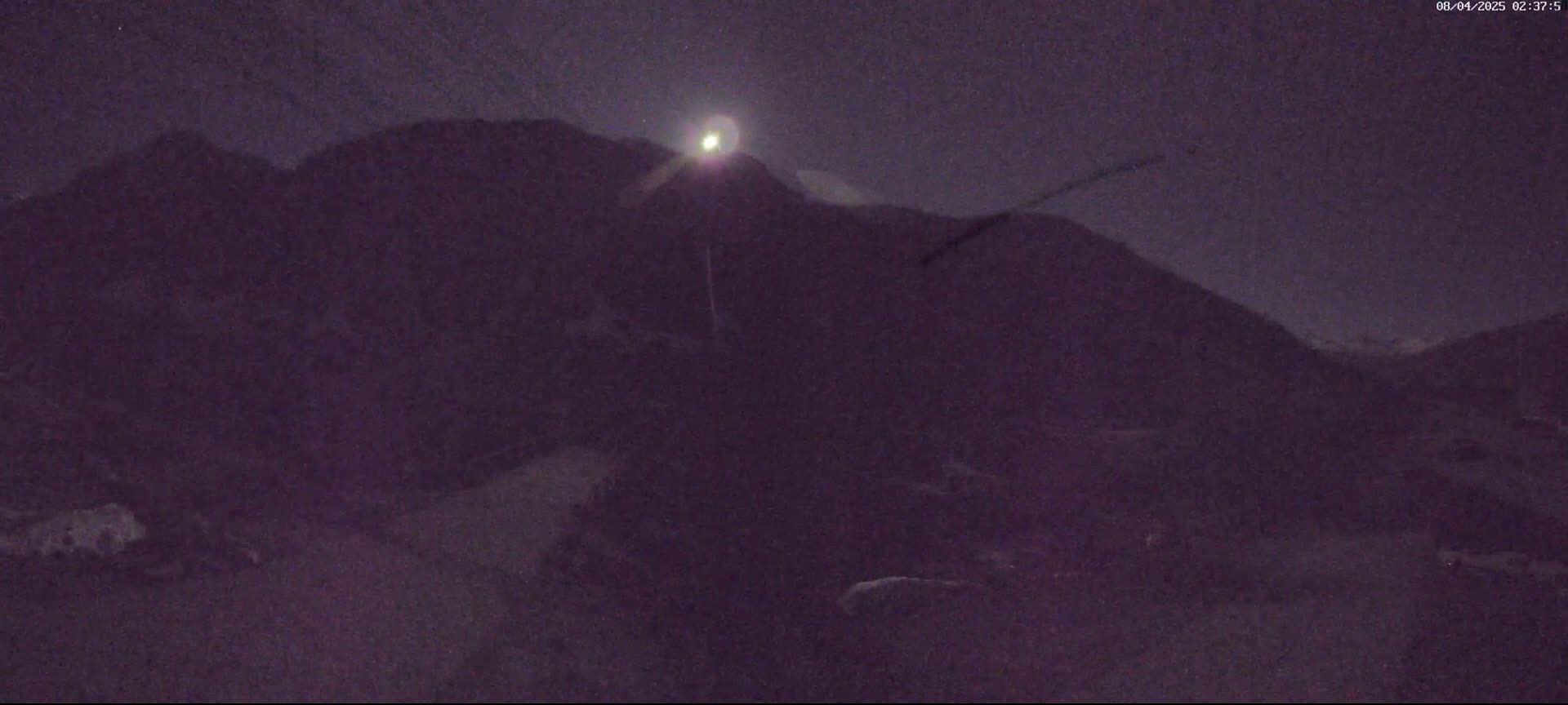 A bright moon illuminates dark mountains under a night sky.