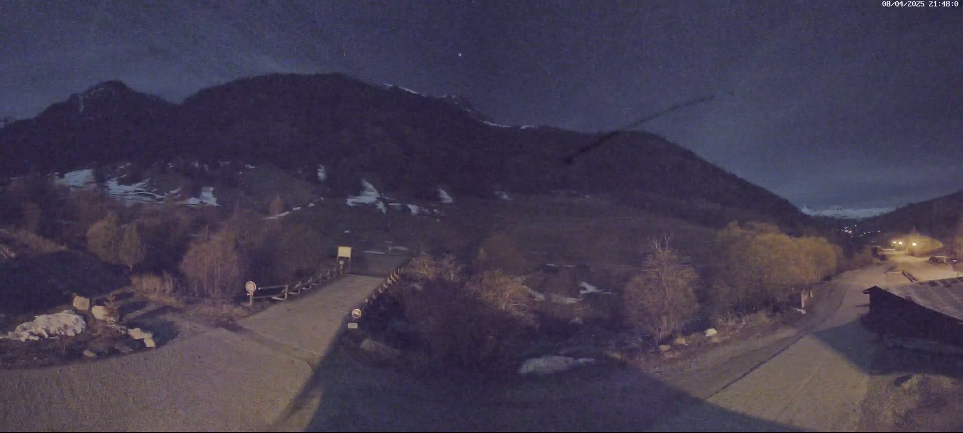 A nighttime view of a small bridge and road leading to a mountainous area under a dark, clear sky.
