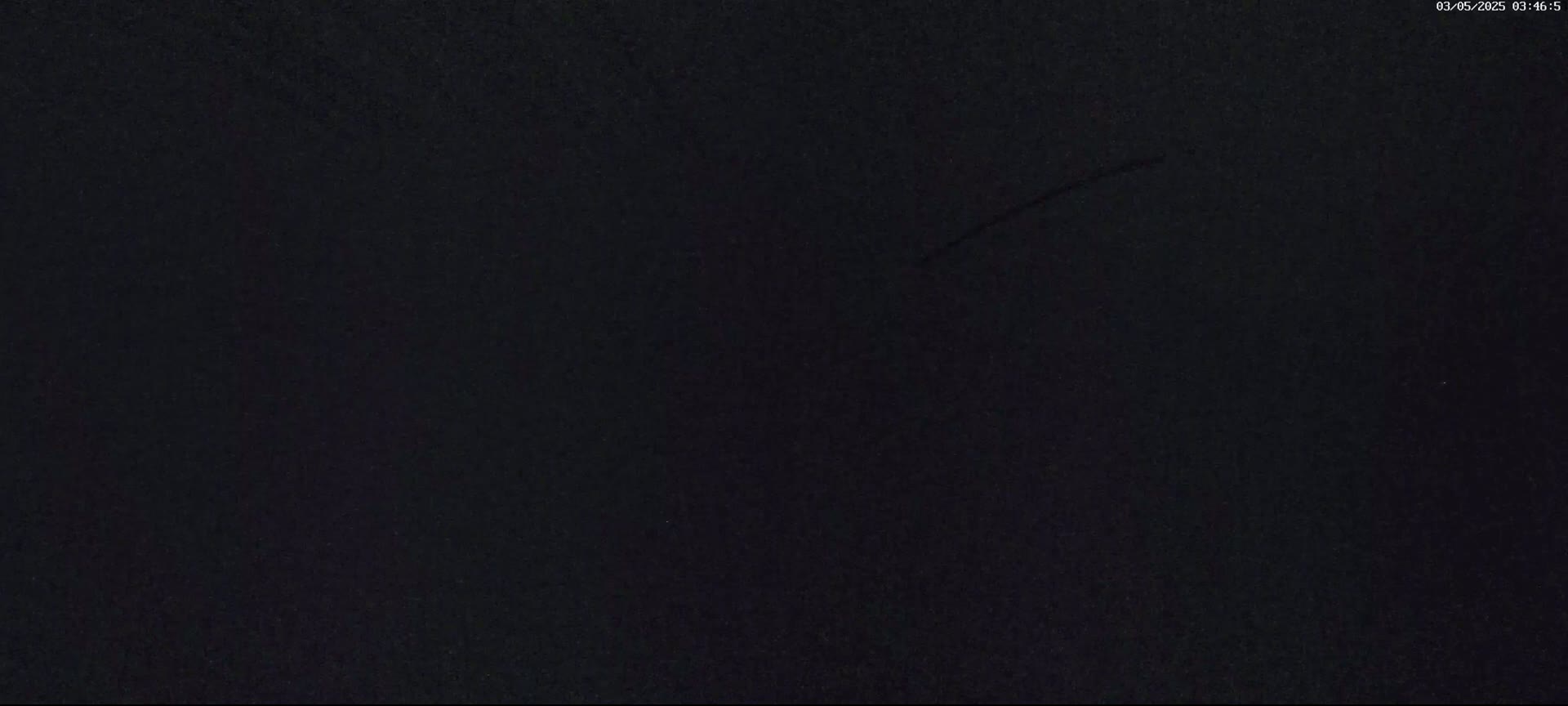 A dark, possibly nighttime image shows a mostly uniform black surface with a faint, thin scratch or mark across it.