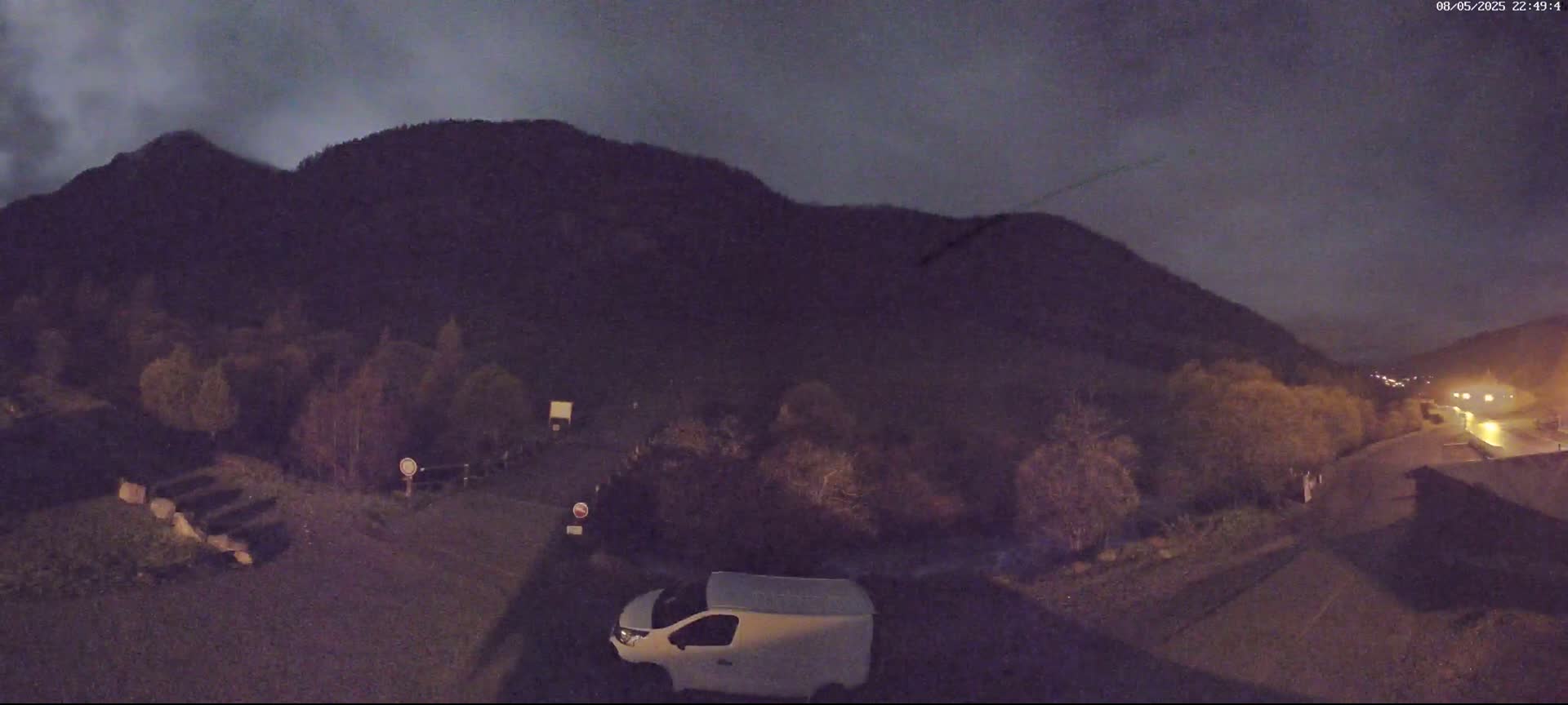 A white van is parked in a dark, nighttime scene, with a large, shadowy mountain in the background under a cloudy sky.