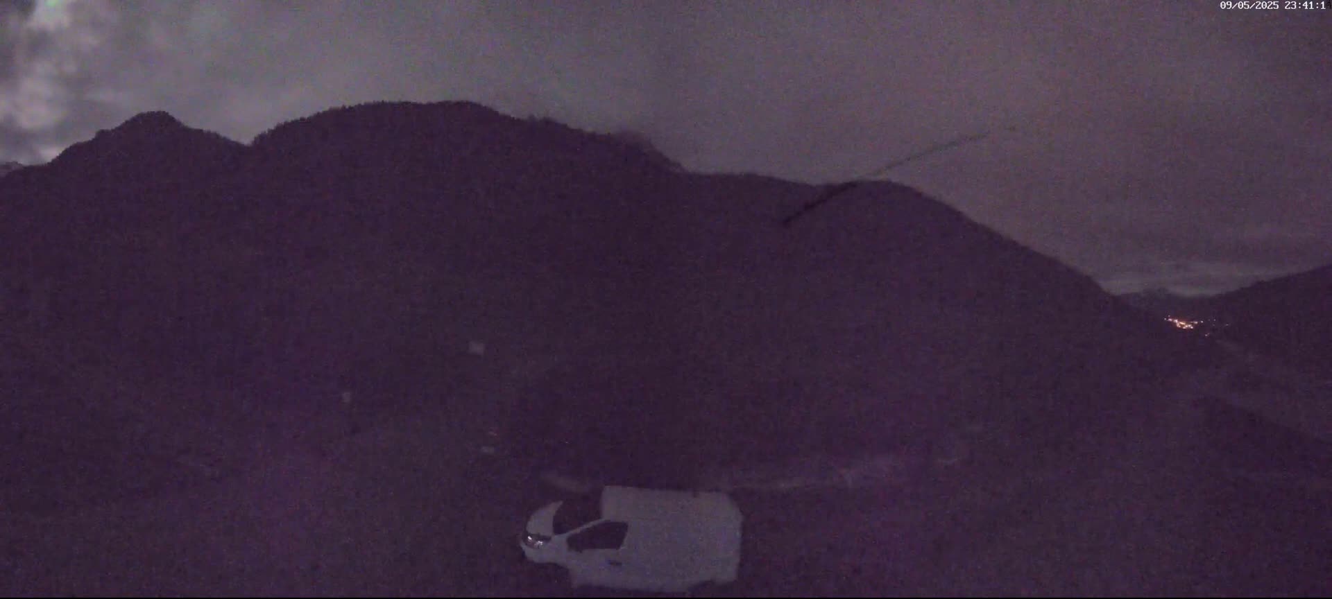 A white van is parked in front of a dark mountain under a cloudy night sky.