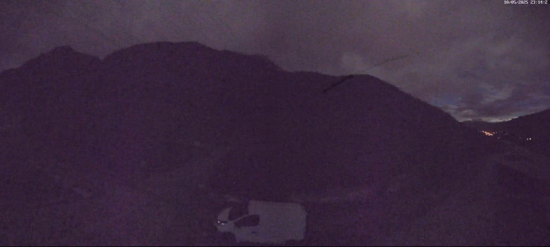 A white van is parked in front of dark mountains under a twilight sky.