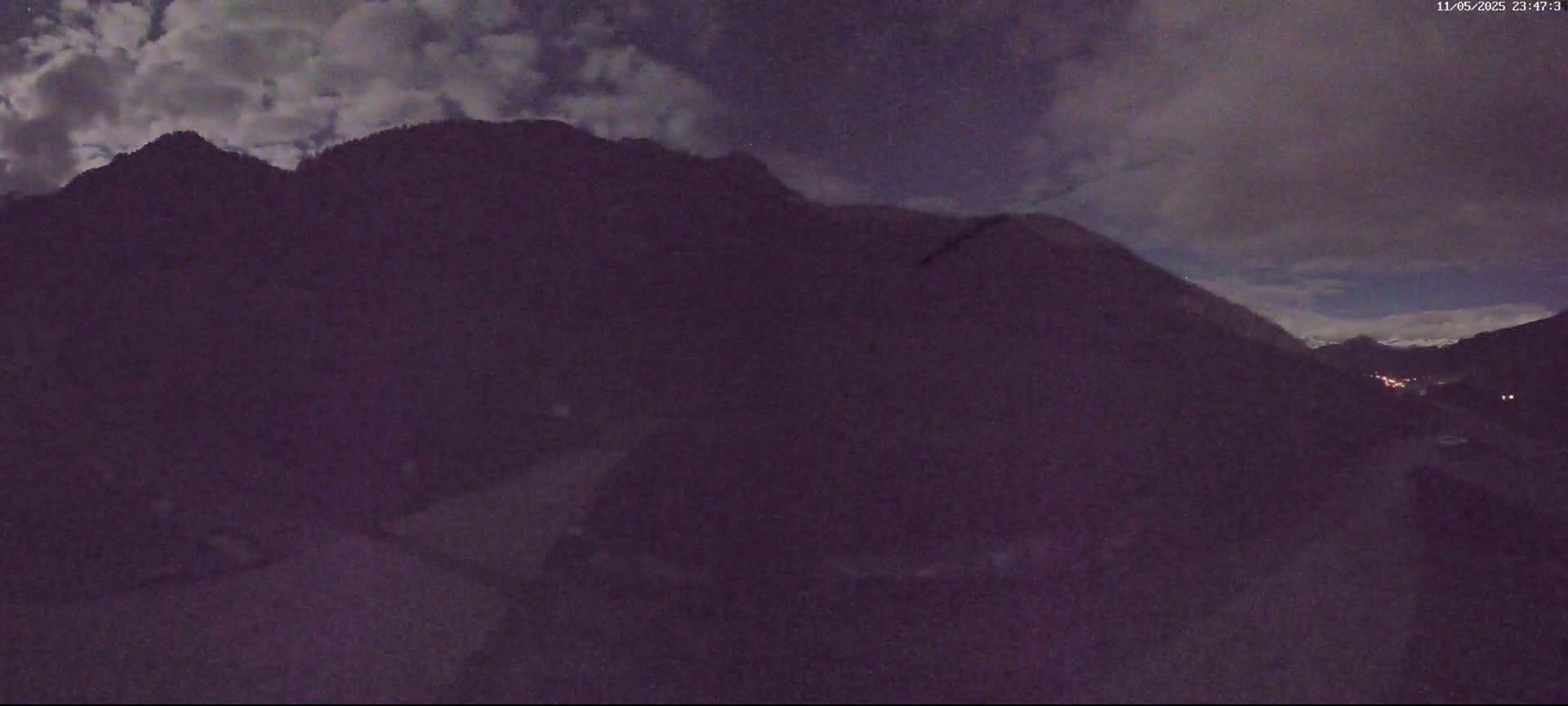 A nighttime view of a dark mountain range under a partly cloudy sky.