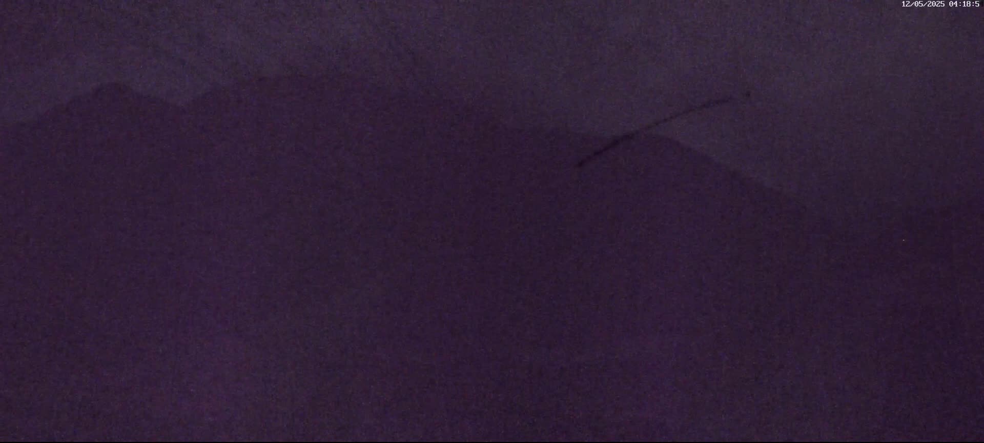 A dark, blurry image shows a mountain range under a nighttime, possibly snowy sky.