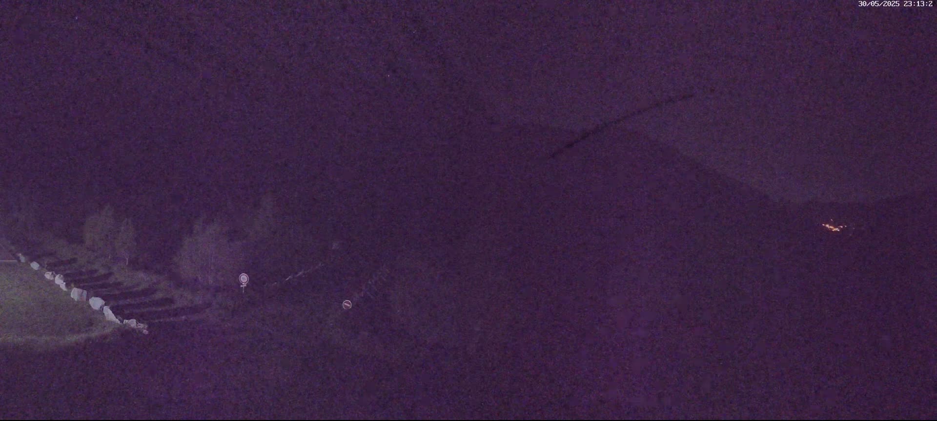 A dark, nighttime scene shows a row of what appears to be tombstones or similar objects along the edge of a grassy area, under a mostly clear, dark purple sky.