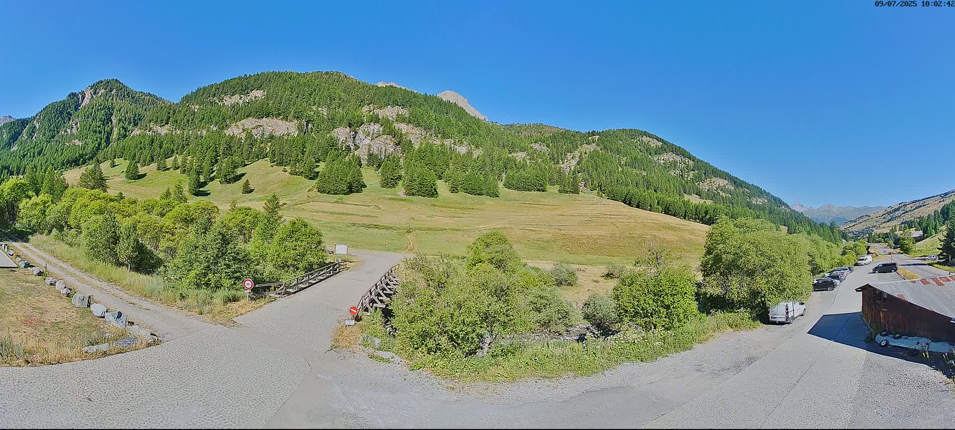 A paved road leads to a grassy valley nestled between mountains under a clear blue sky.