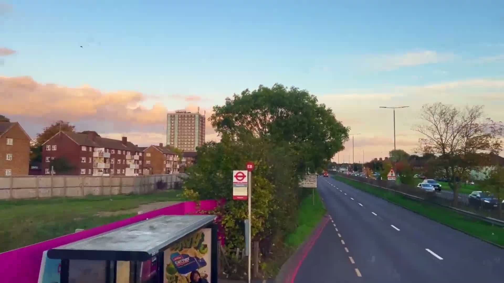 A multi-lane road with cars driving on it under a partly cloudy sunset sky, next to residential buildings and a bus stop.