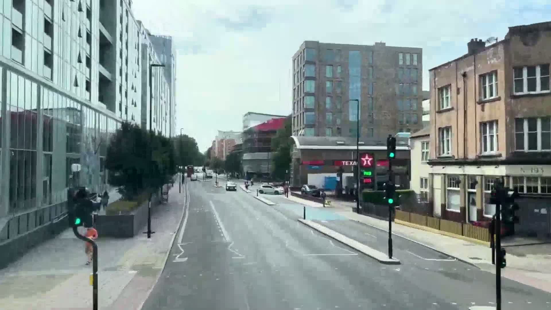 A mostly empty city street lined with modern and older buildings on a cloudy day, with a few pedestrians and cars visible.