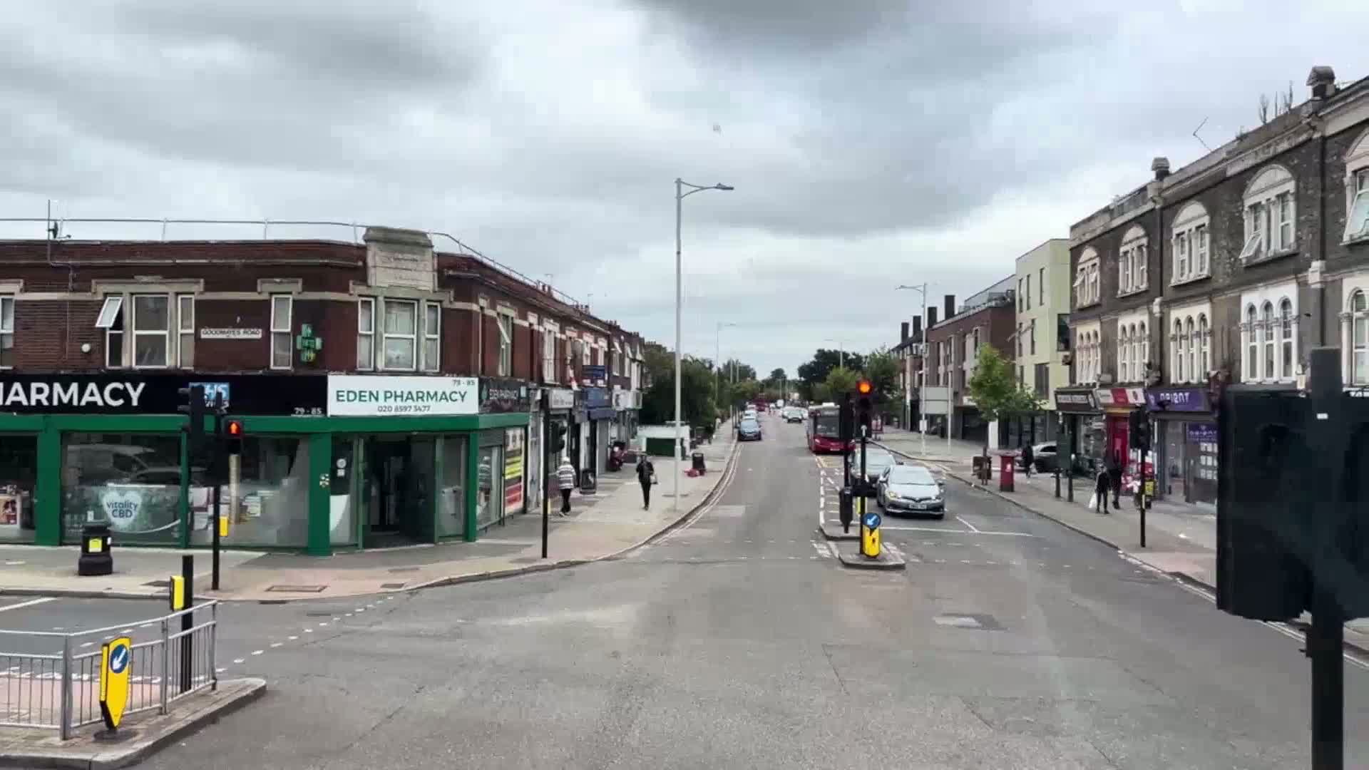 A street scene on an overcast day shows a multi-lane road with cars and pedestrians, lined with two-story brick buildings that include shops.