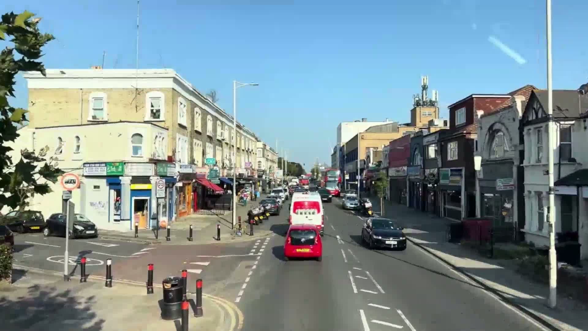 A sunny day reveals a street scene with two-story shops and buildings lining both sides of a road, where several cars are driving.