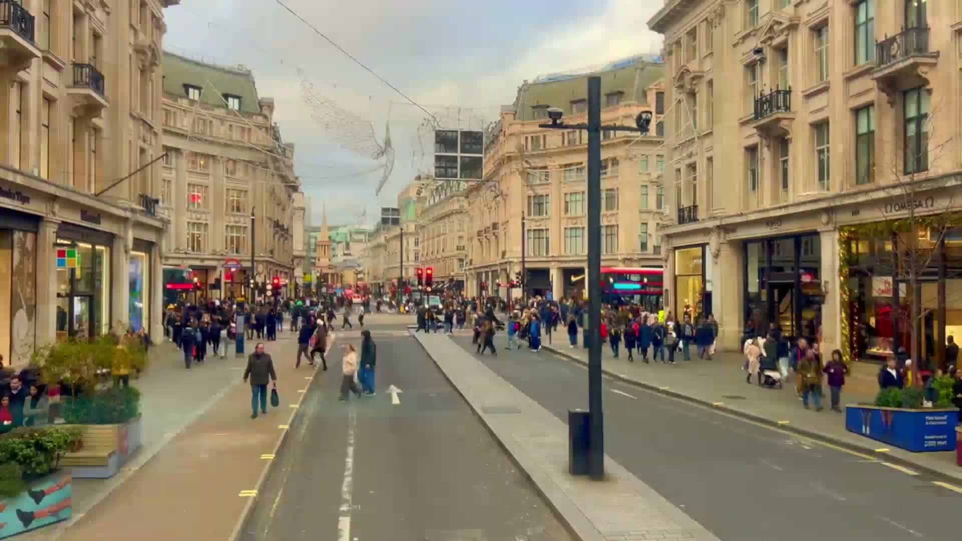A bustling city street filled with pedestrians and shops, under a cloudy sky.